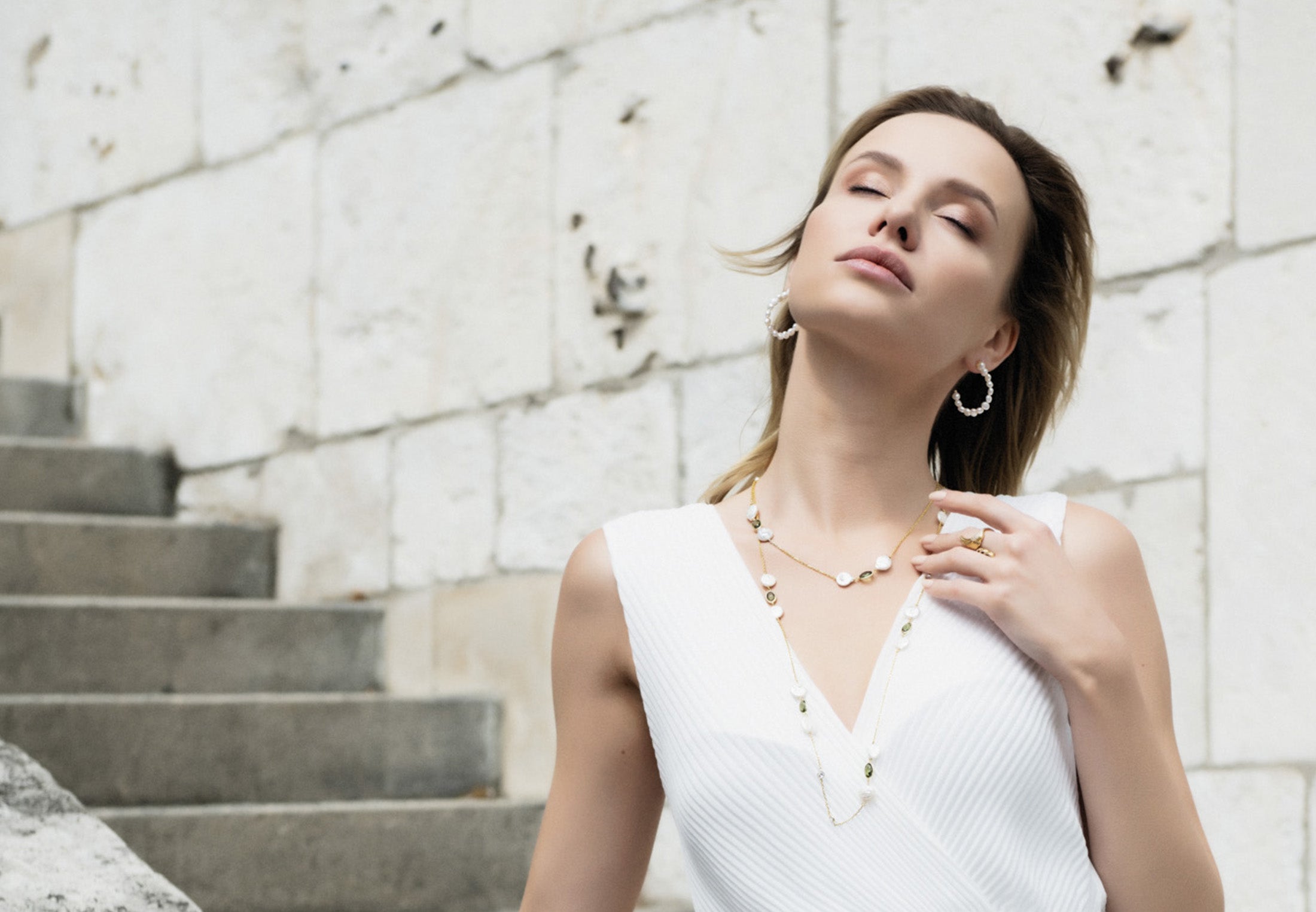 Pearl jewellery with gemstones, worn by model outside in sunshine