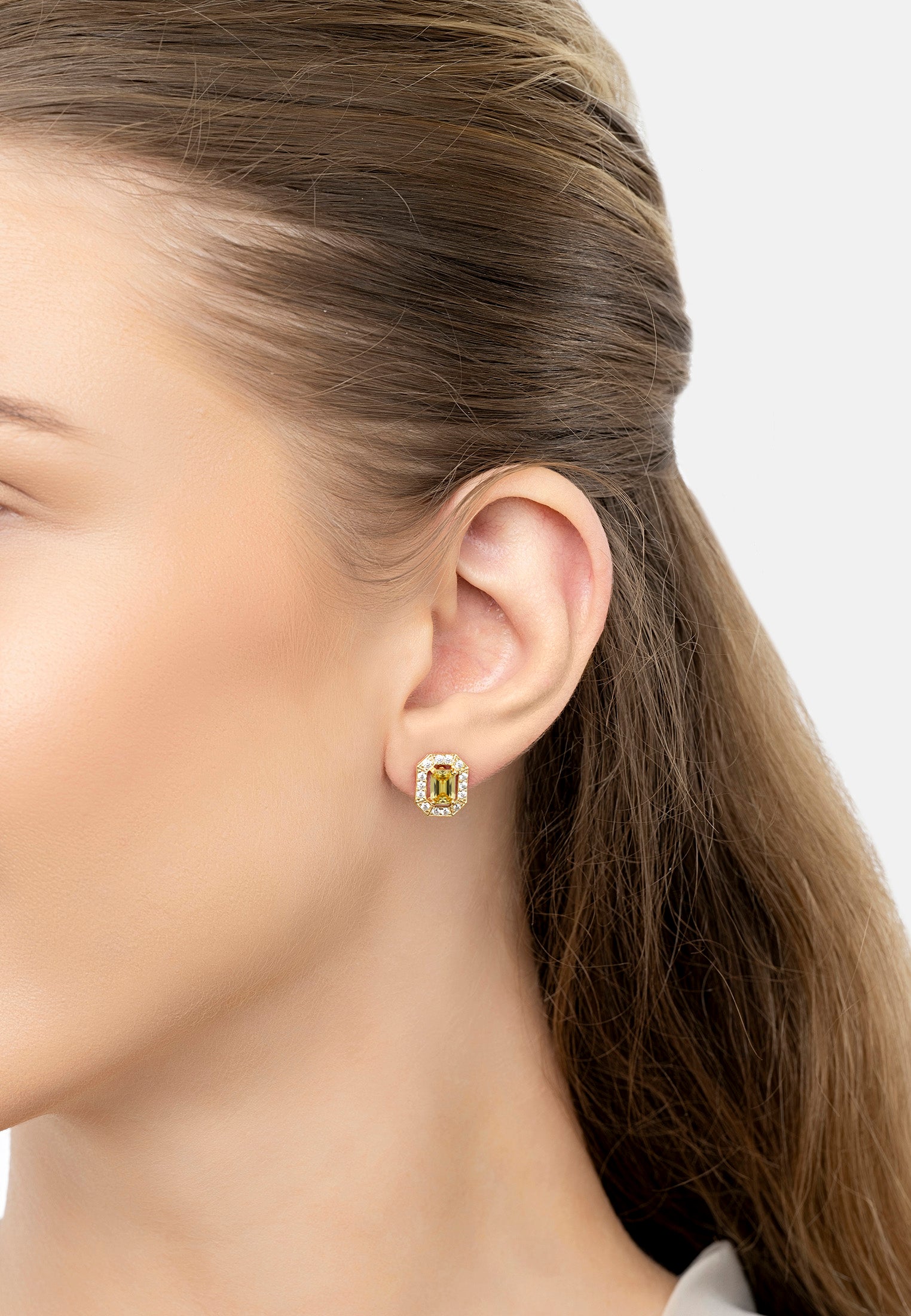 Close-up of a woman wearing green gemstone earrings with a neutral background