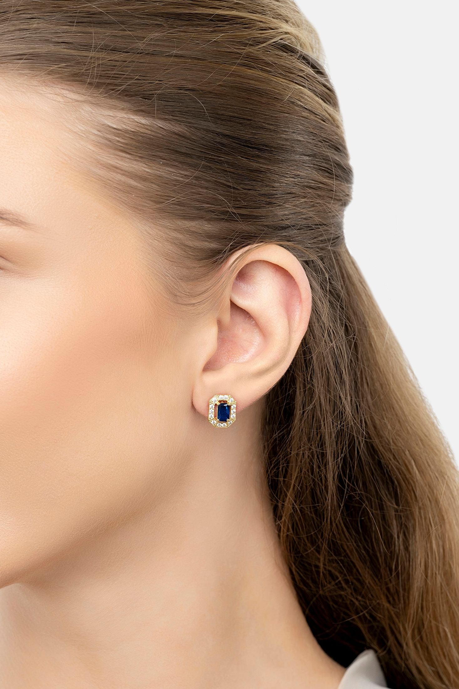 Close-up of a woman wearing blue gemstone earrings with a neutral background
