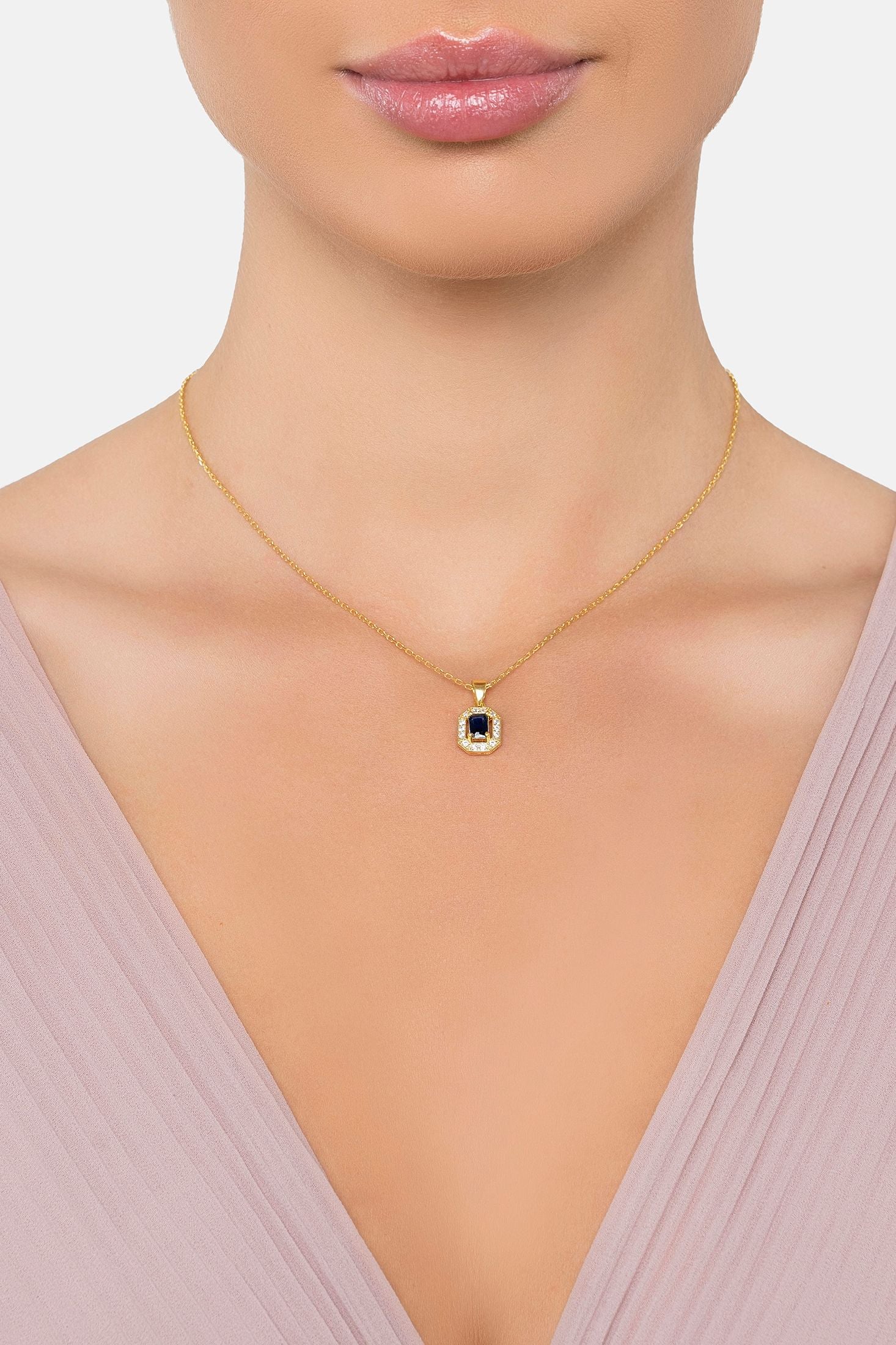 Gold necklace with a blue pendant on a model wearing a light pink top.