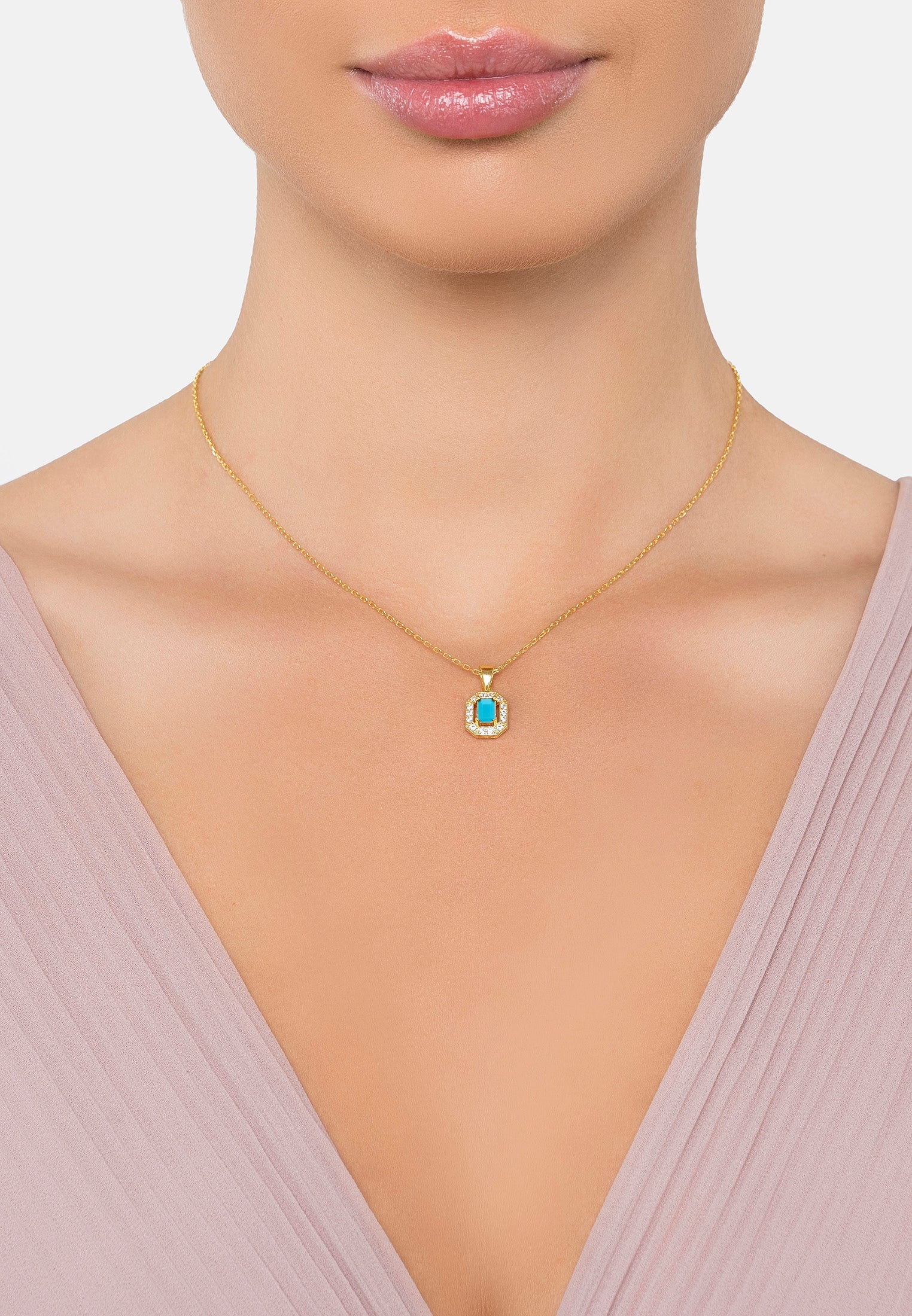 Gold necklace with a turquoise gemstone pendant on a model wearing a light pink top.