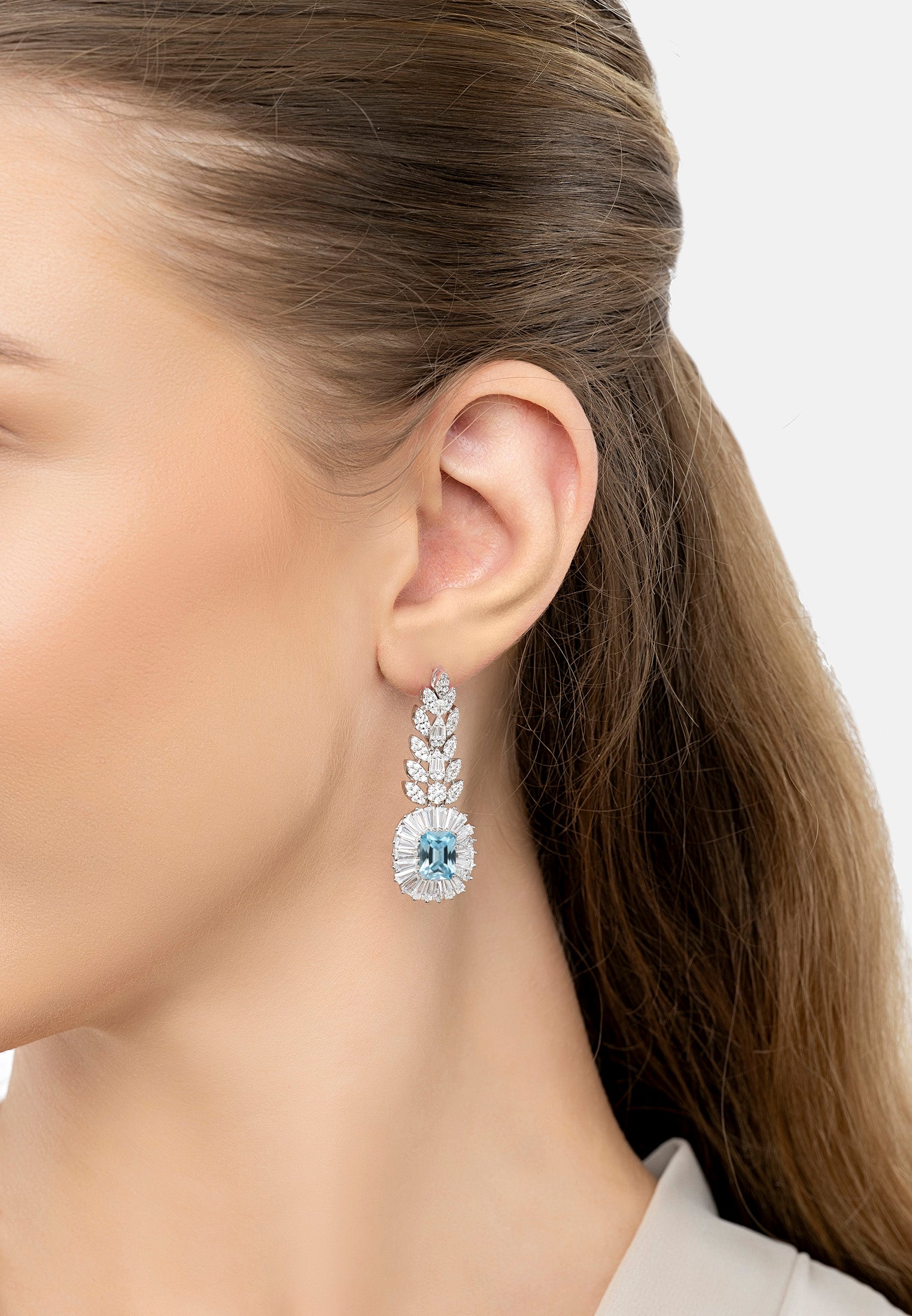 Close-up of a woman wearing a diamond earring with a blue gemstone on a neutral background