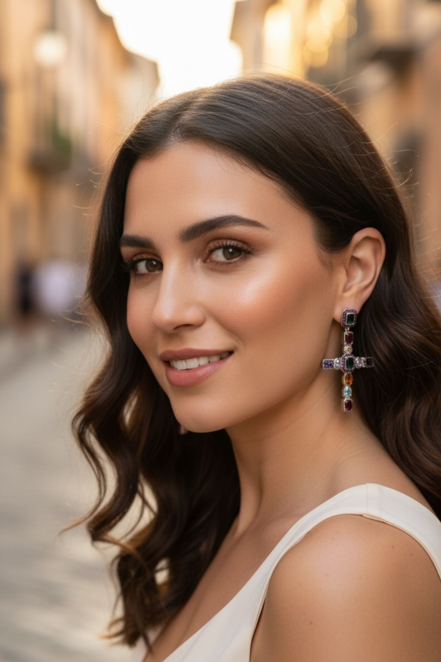 Woman with styled hair and large cross earrings with multicoloured gemstones in an urban setting