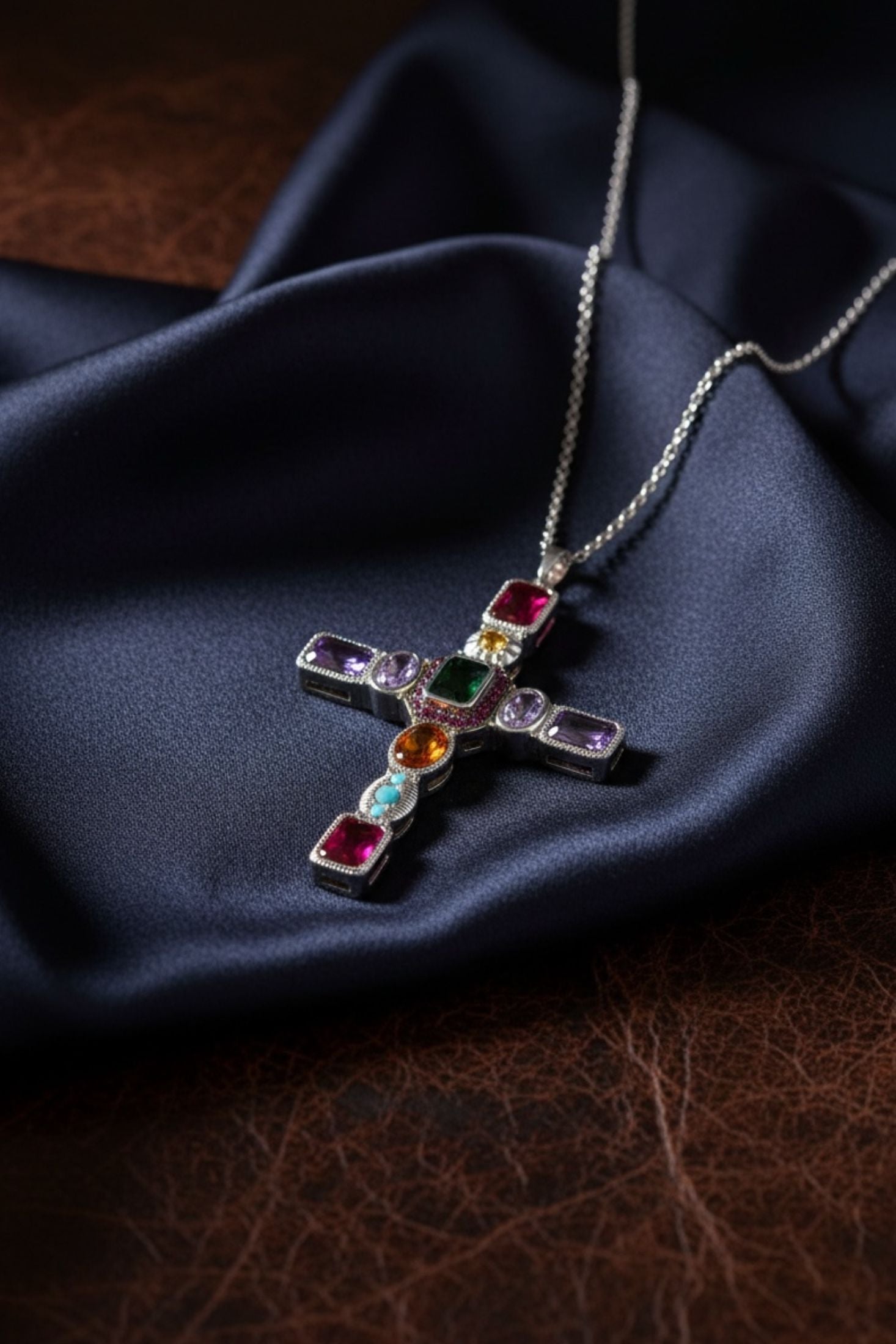 Cross-shaped necklace with colorful gemstones on a dark fabric background