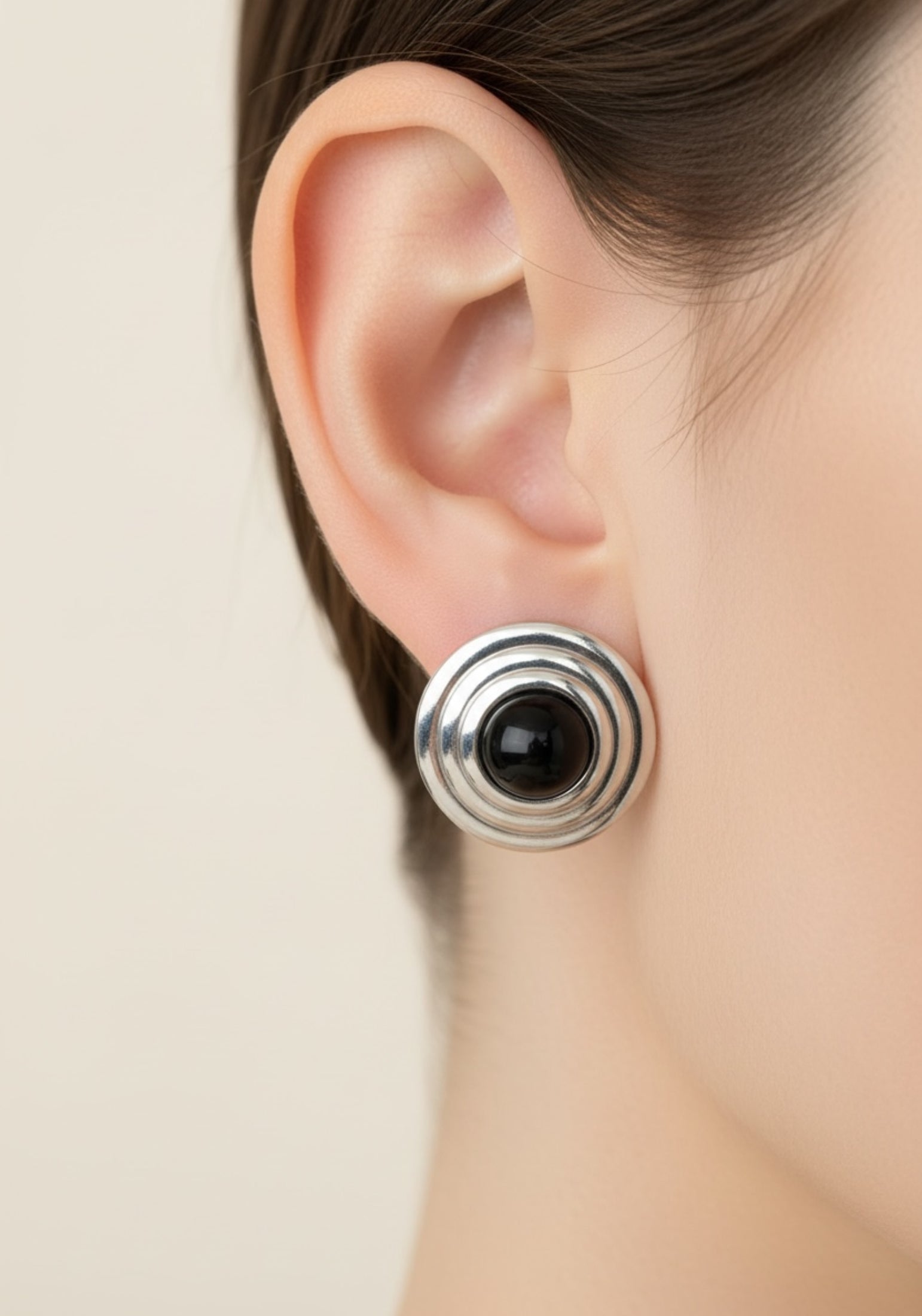 Close-up of an ear wearing a silver and black earring against a neutral background