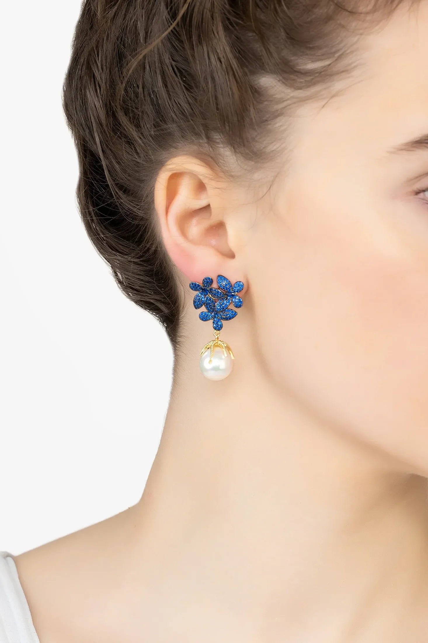 Angled view of Flowers Pearl Earrings Sapphire Blue Gold, showing flower design, pearl and sapphire detailing, gold finish and the jewellery profile.