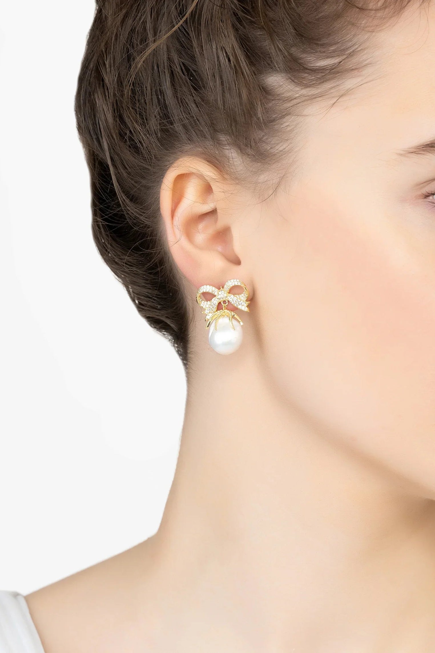 Pearl earring with gold bow detail worn by a model on a white background