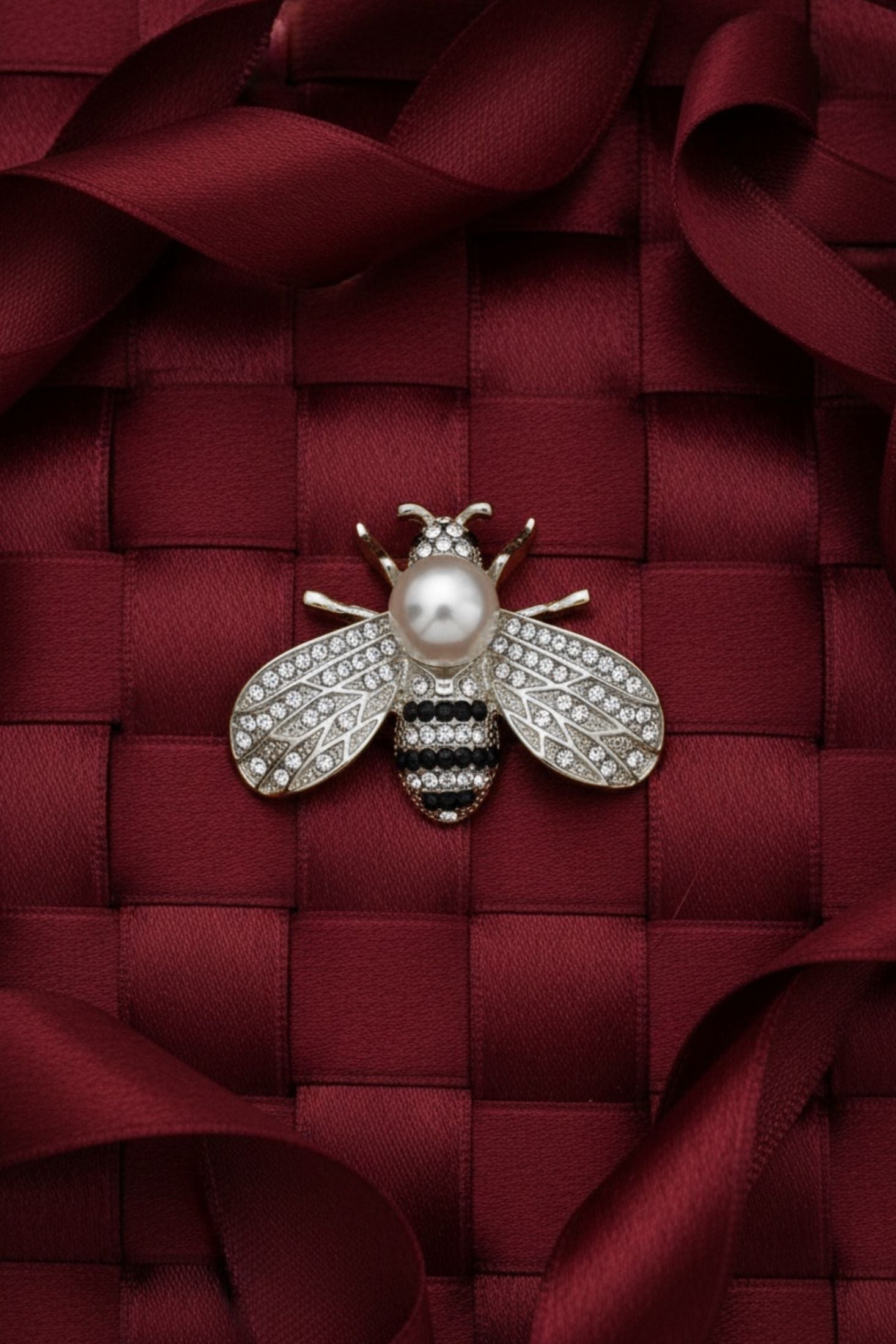 Decorative bee brooch with pearl on a red textured fabric background