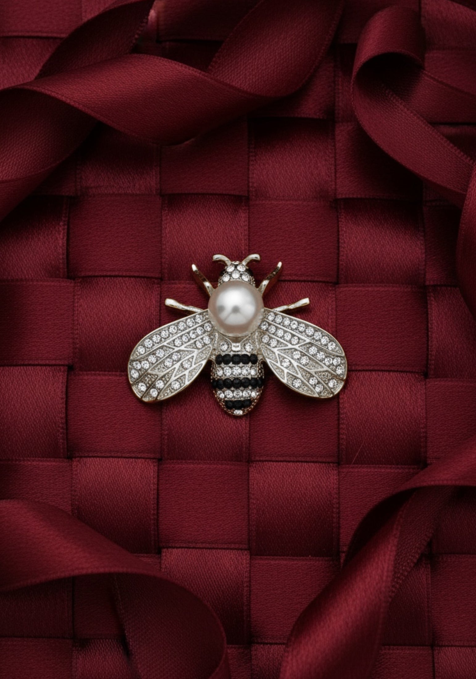 Decorative bee brooch with pearl on a red textured fabric background