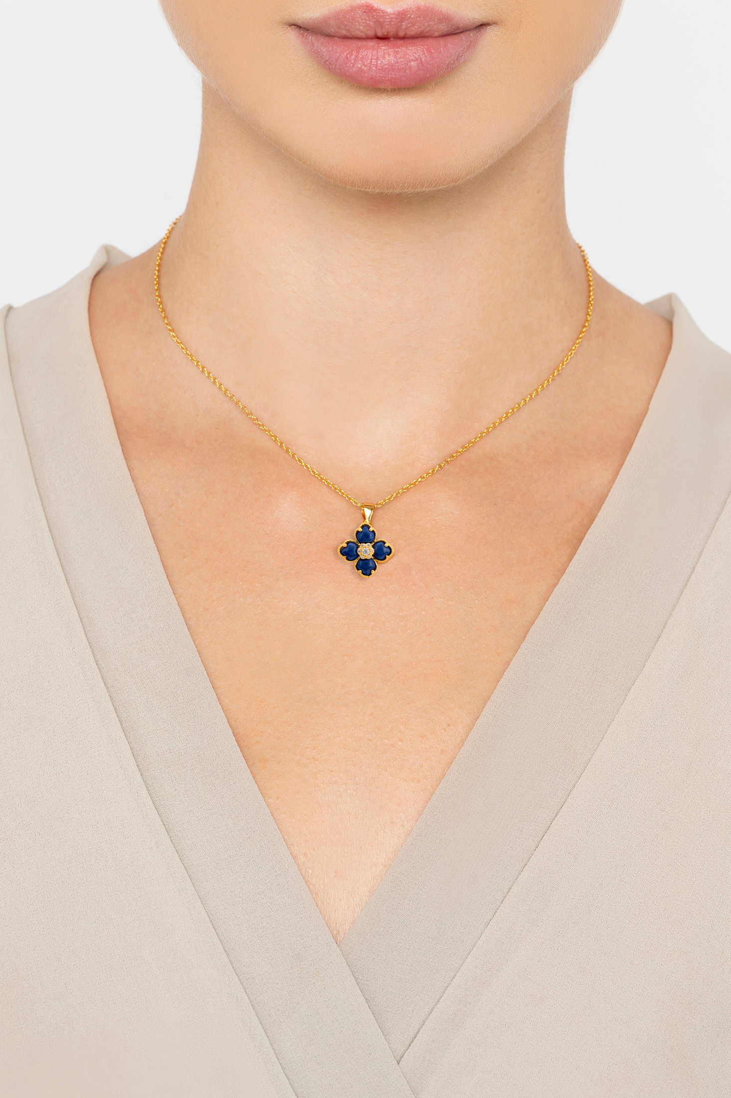 Gold necklace with a blue pendant worn by a person in a beige top.