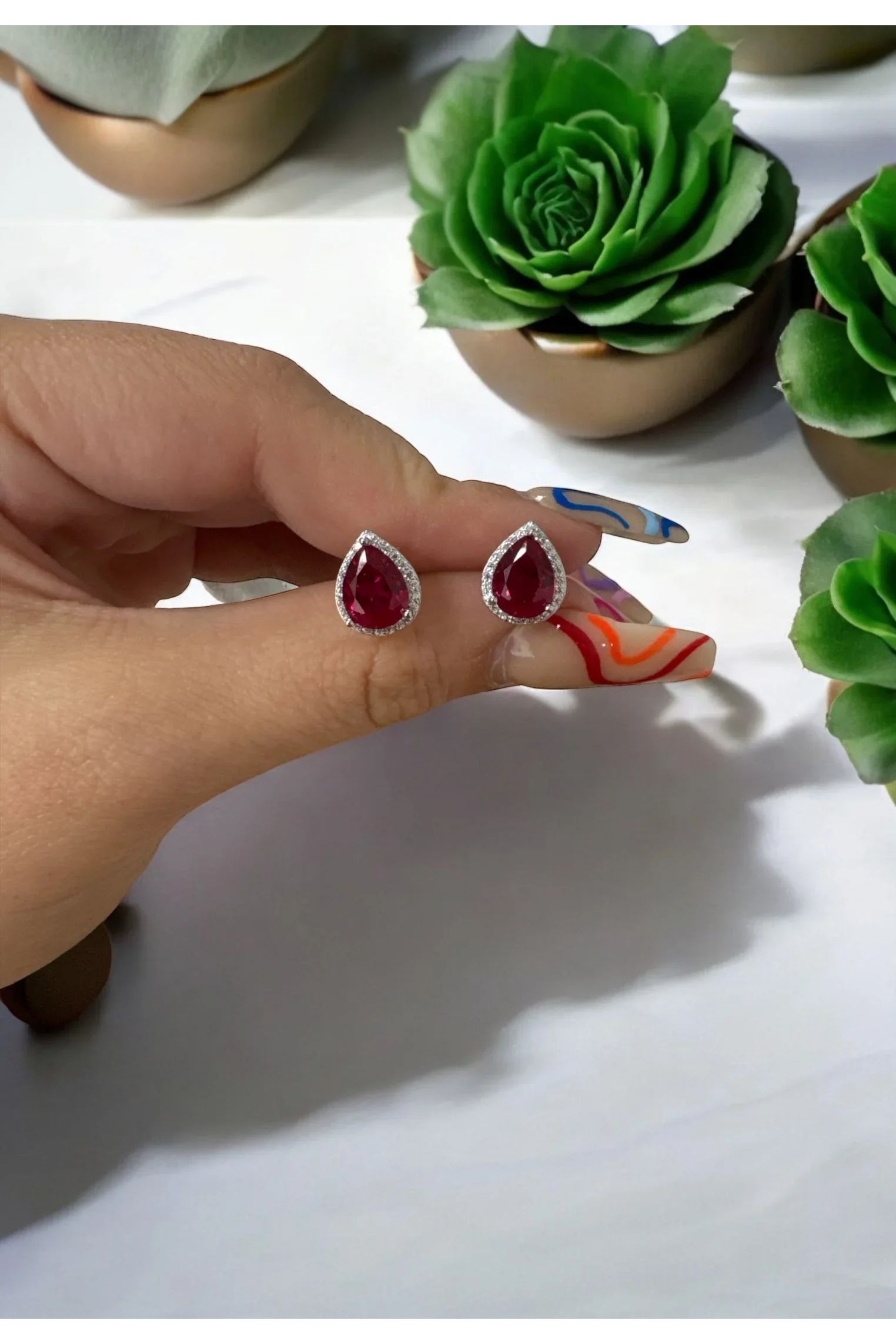 The earrings held up by a hand model.