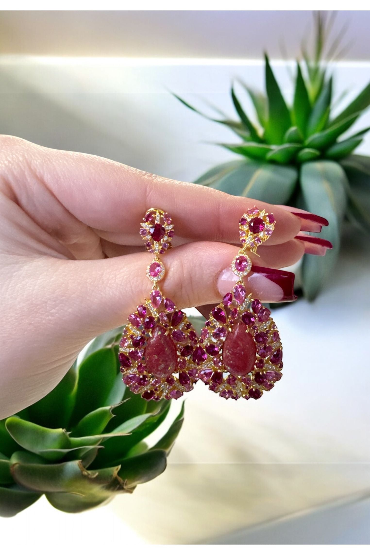 The earrings held up by a hand model.