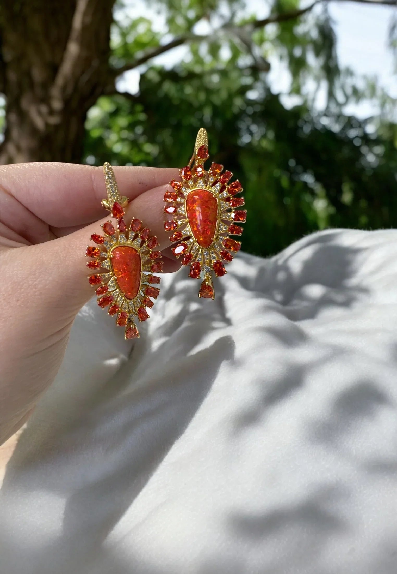 The earrings held up by a hand model.
