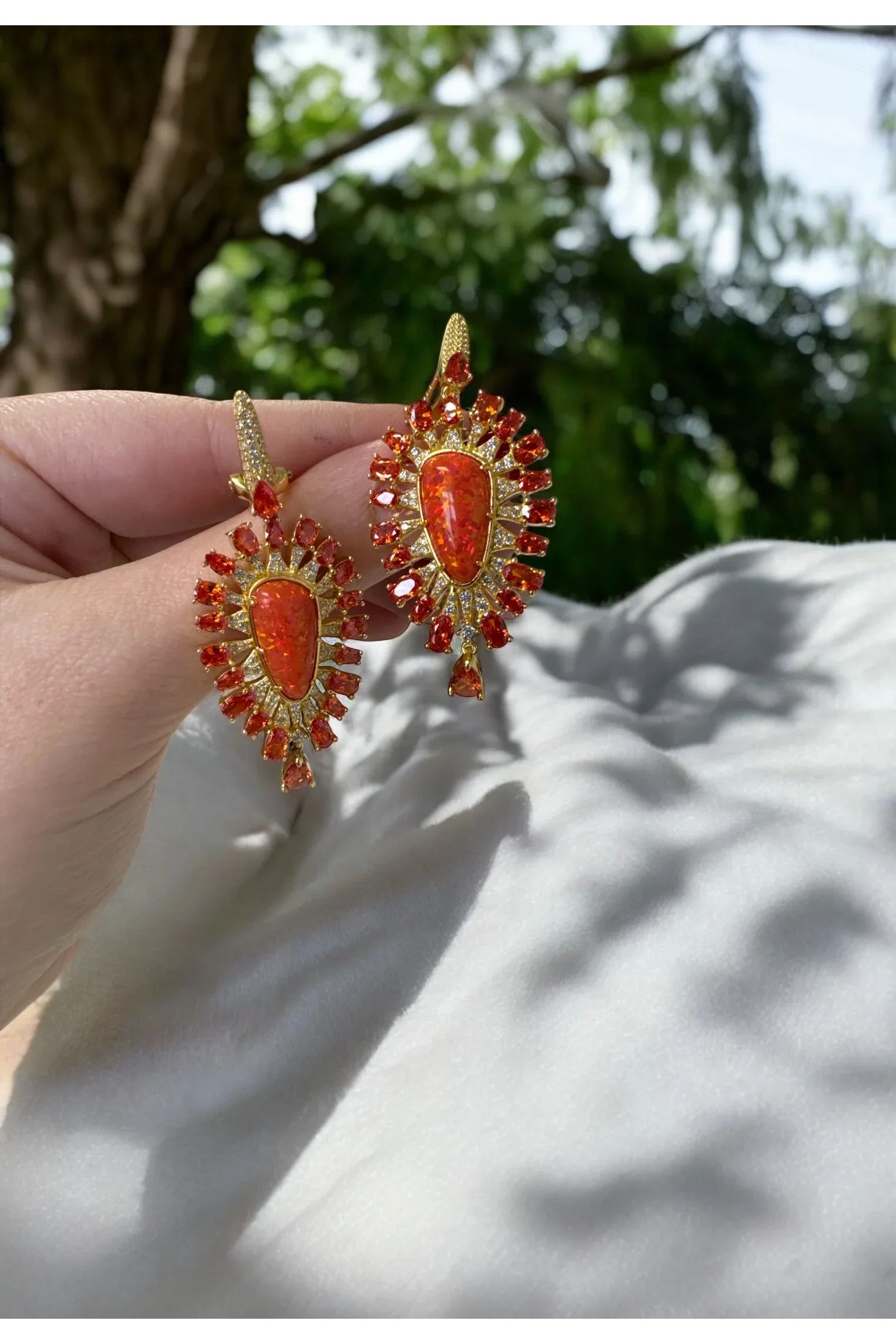 The earrings held up by a hand model.