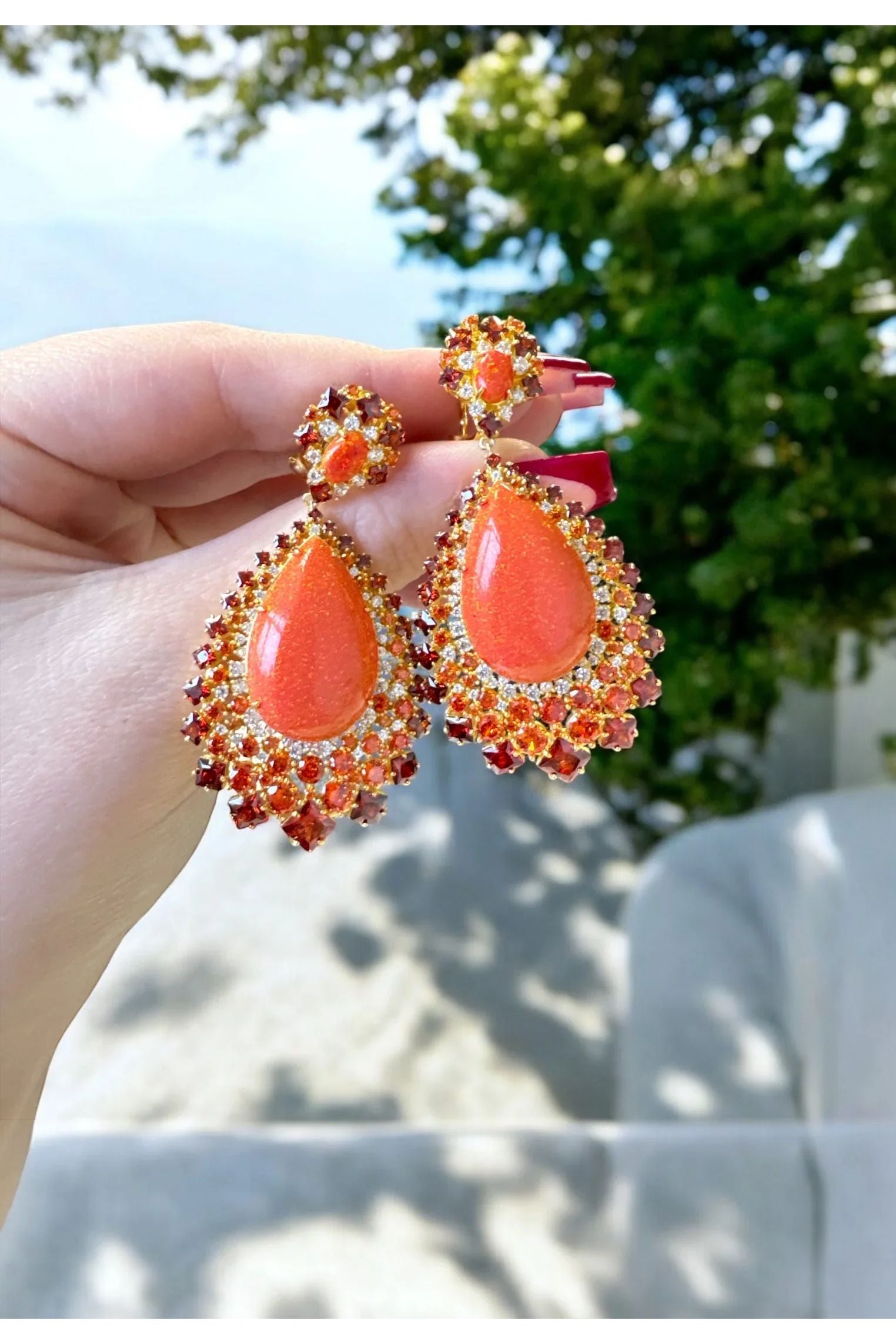 The earrings held up by a hand model.