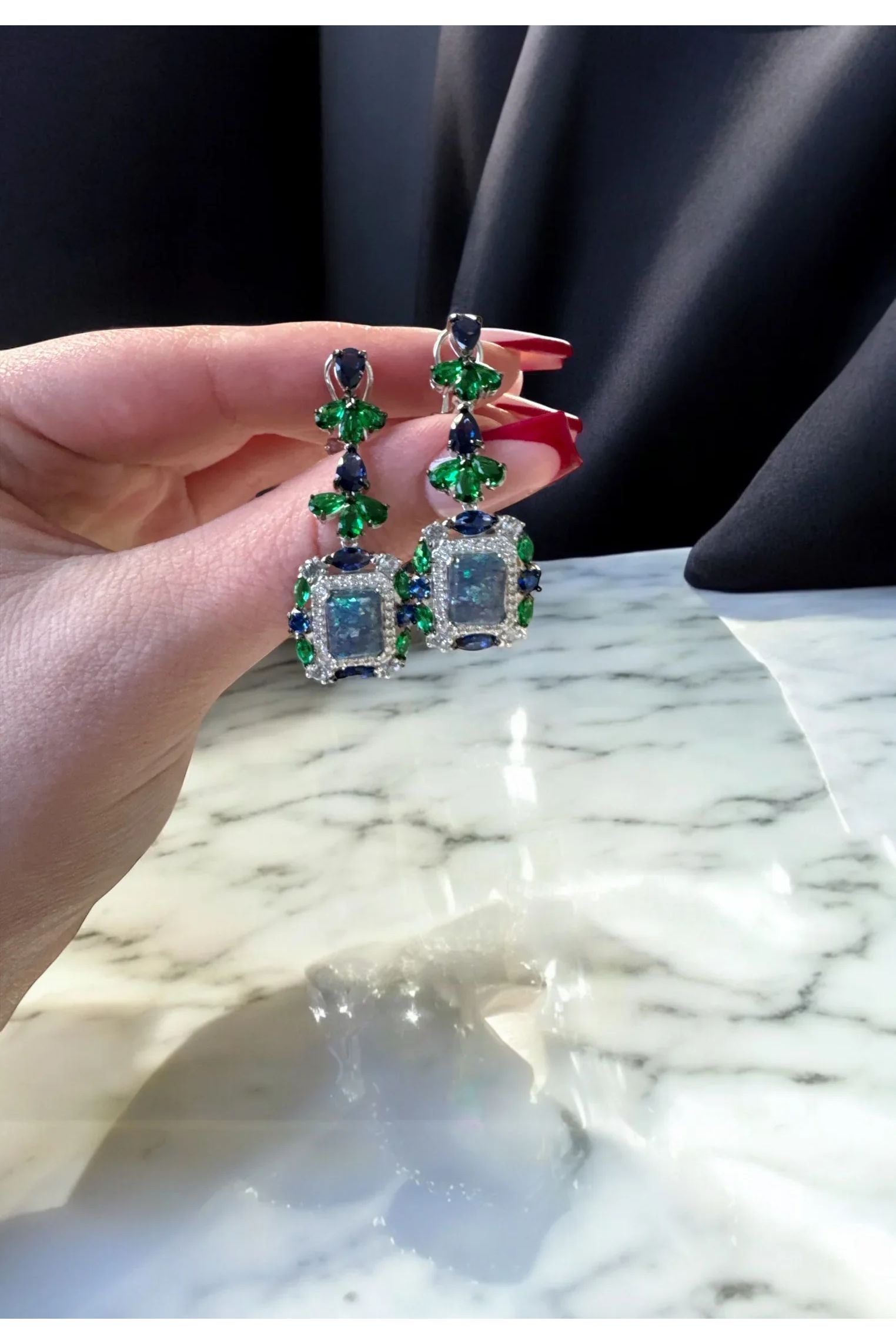 The earrings held up by a hand model.