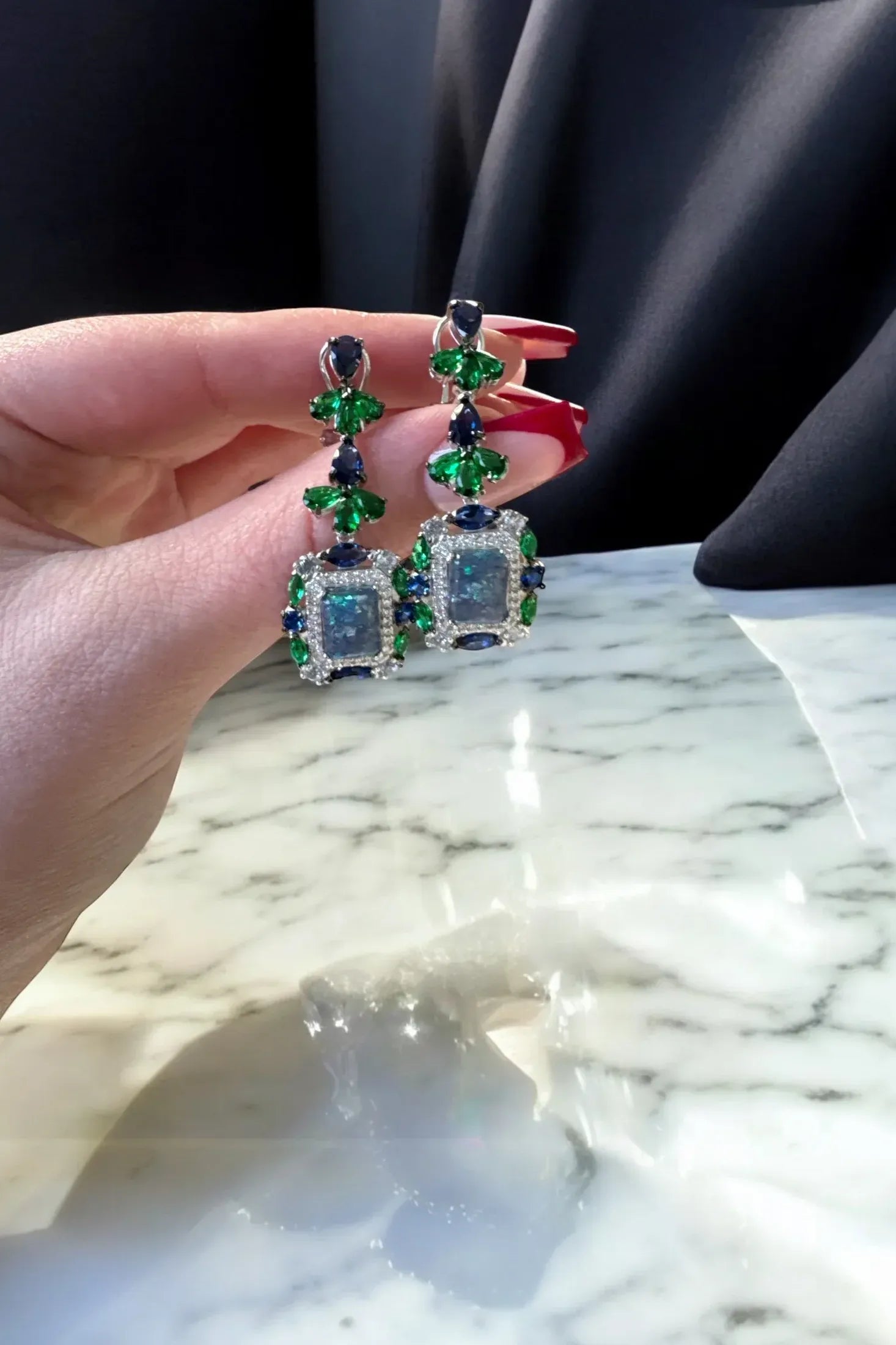 The earrings held up by a hand model.