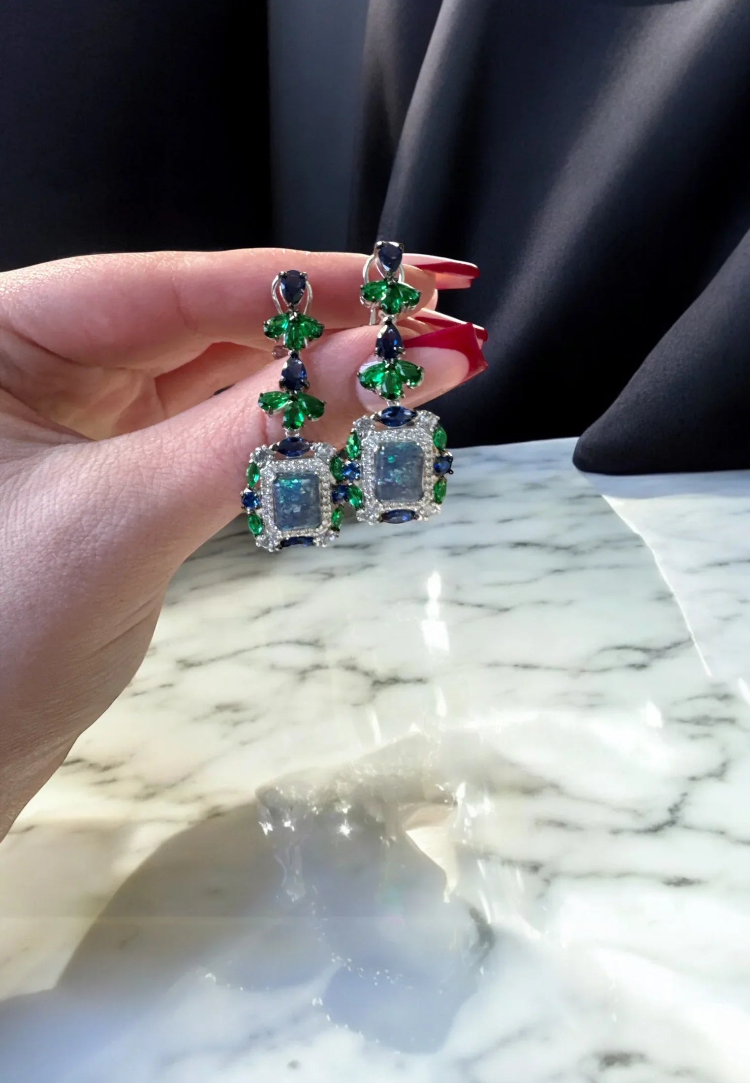 The earrings held up by a hand model.