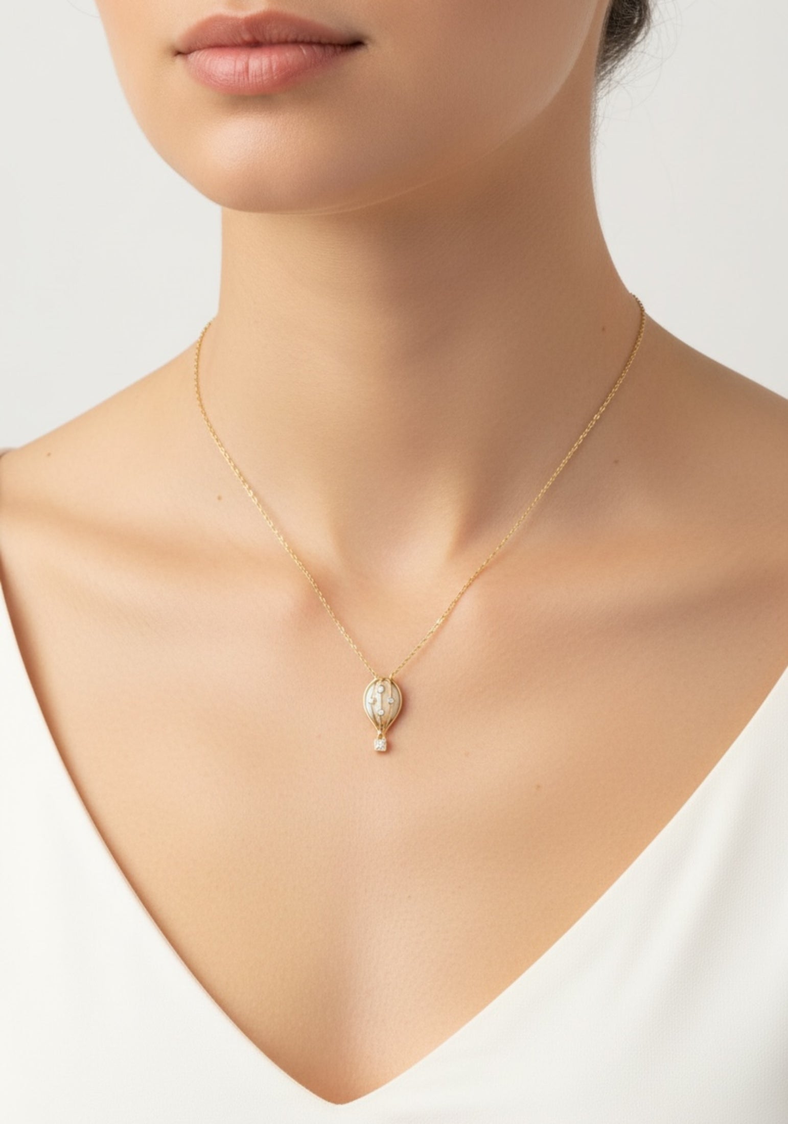 Gold necklace with a hot air balloon pendant on a model against a white background