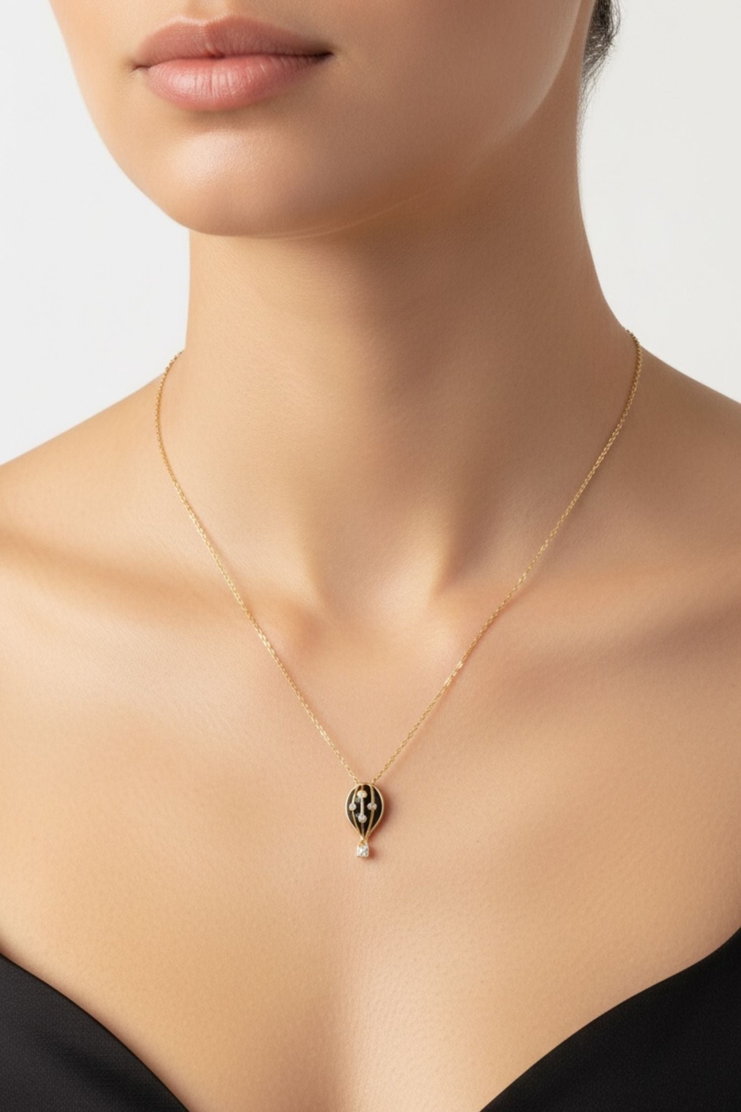 Gold necklace with a black hot air balloon pendant on a model against a neutral background