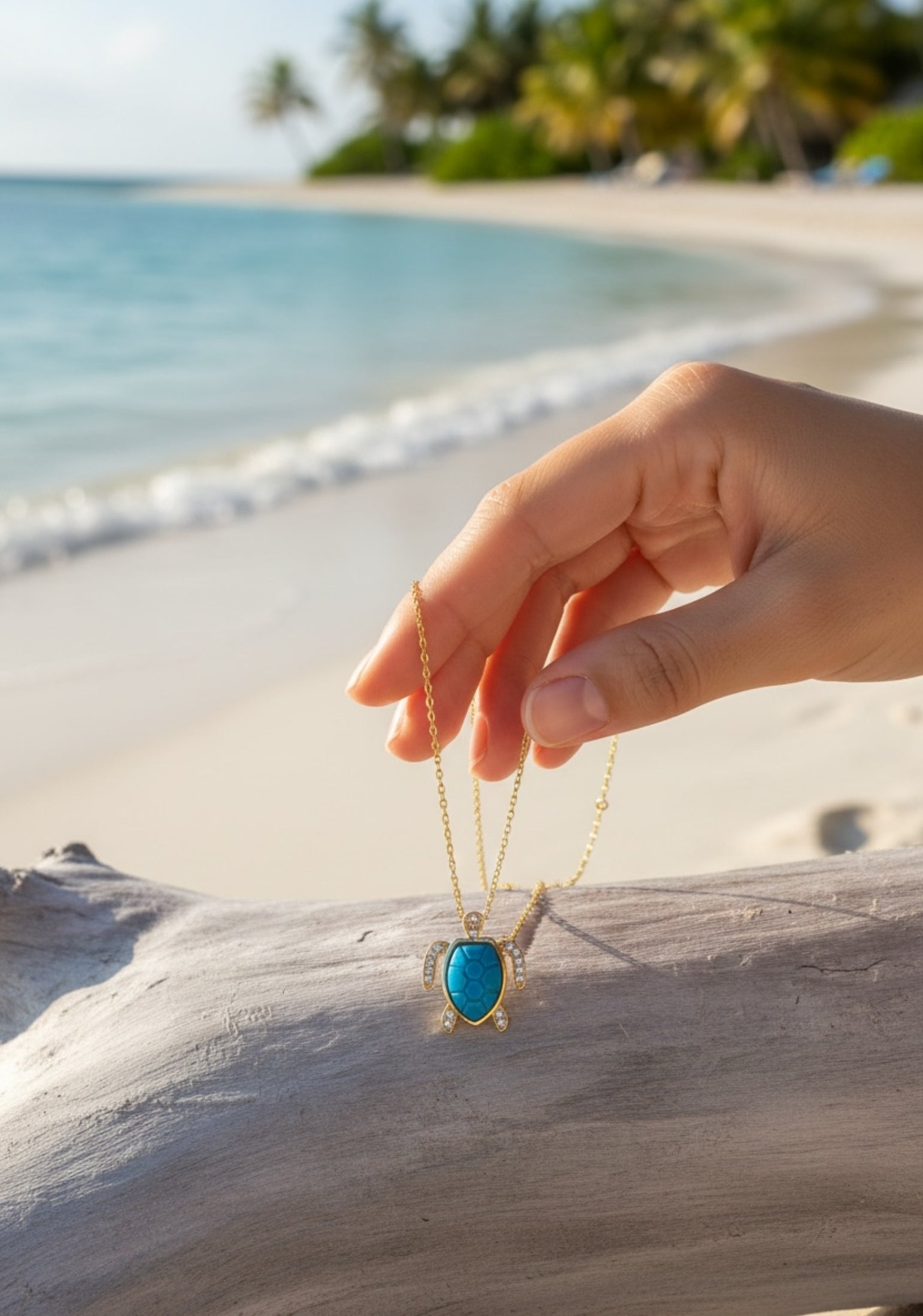 Hand holding a turquoise turtle pendant necklace on a beach