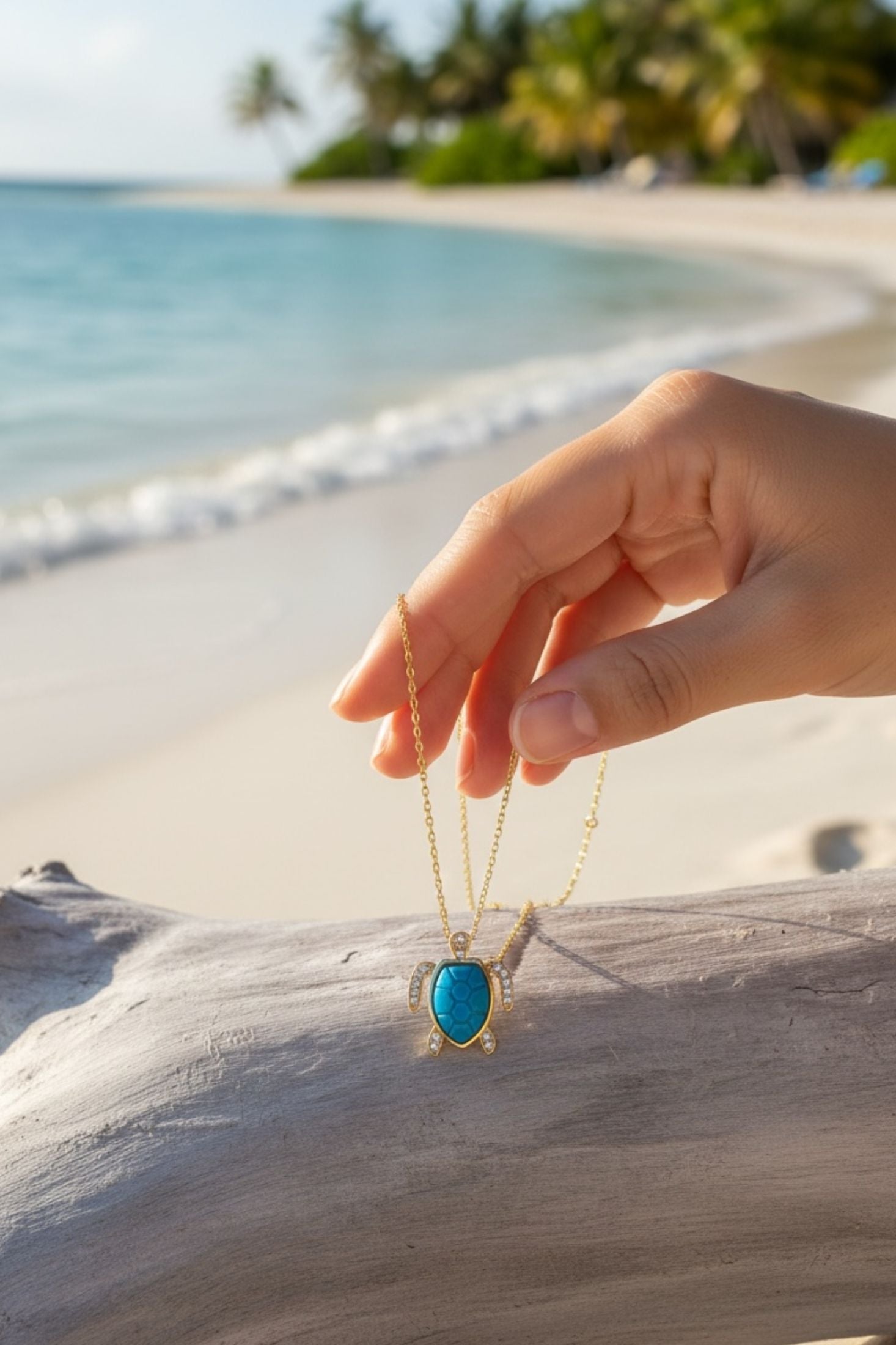 Hand holding a turquoise turtle pendant necklace on a beach