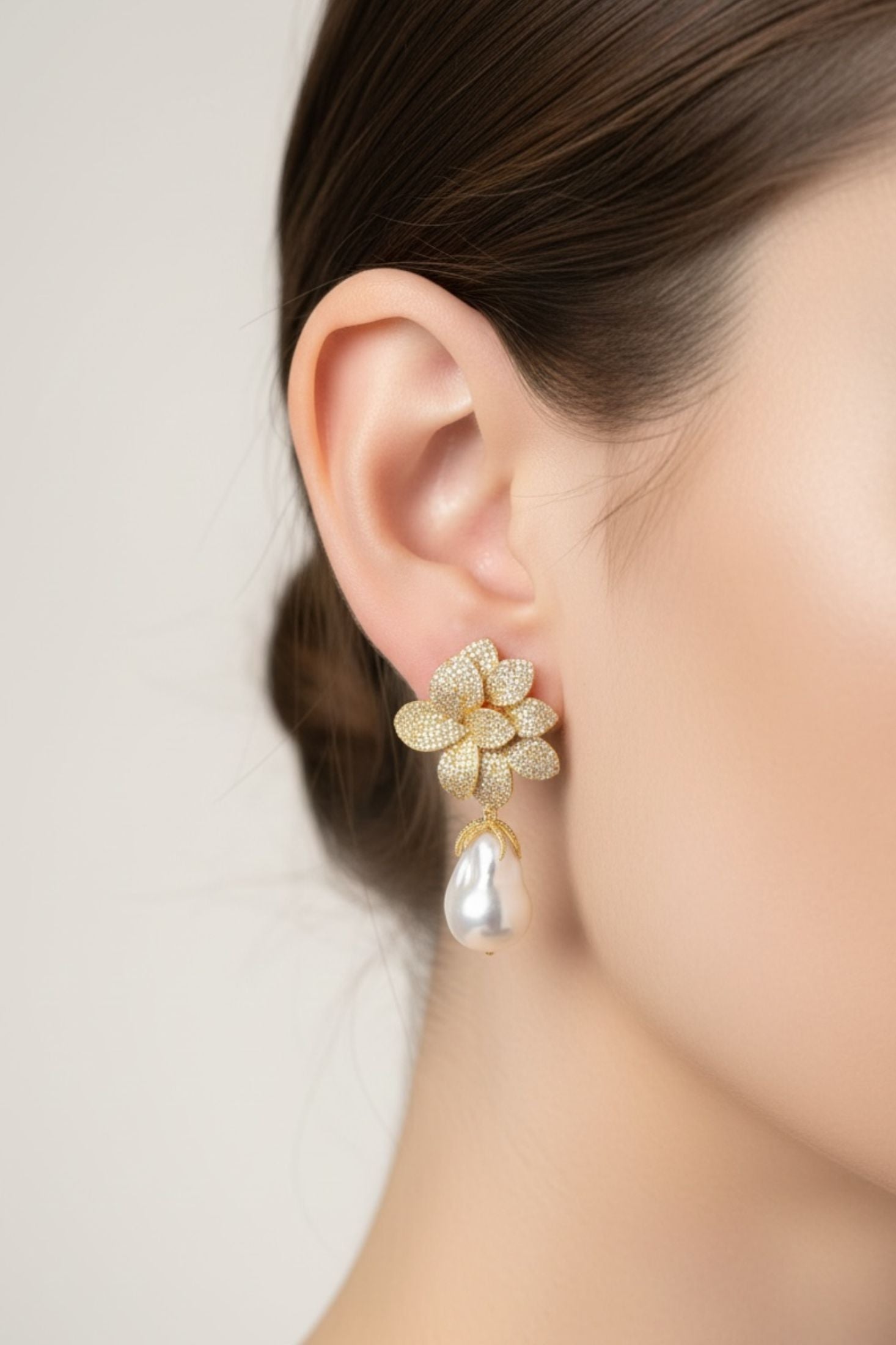 Gold floral earring worn by a person on a plain background