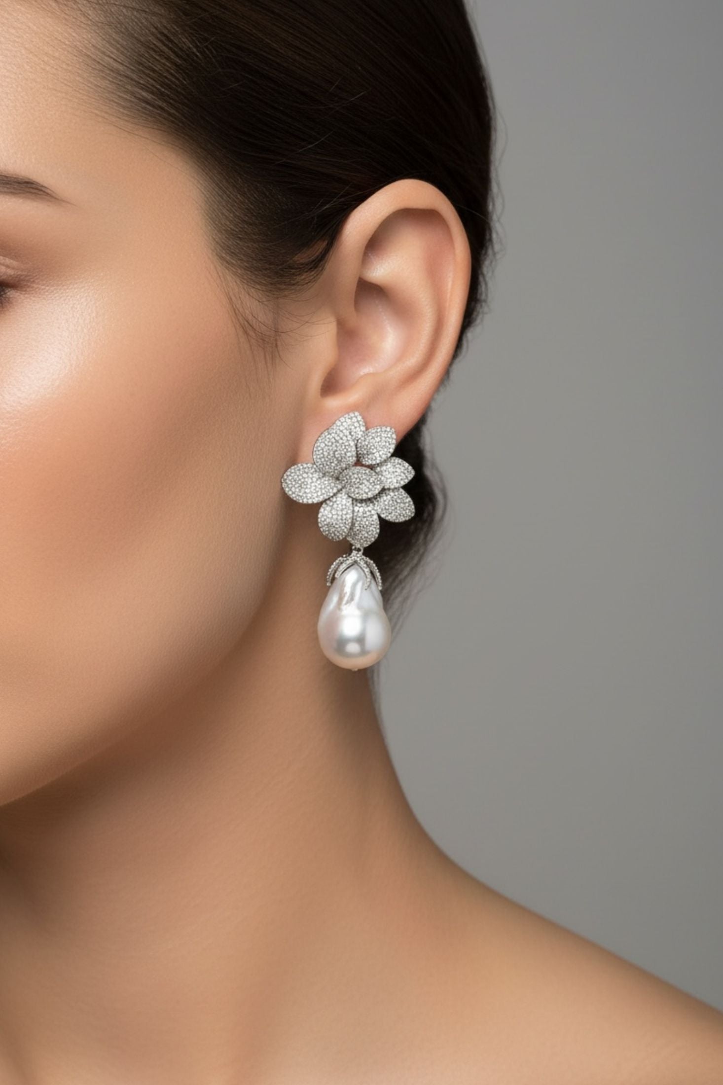 Close-up of a woman wearing a floral earring with a pearl drop on a gray background