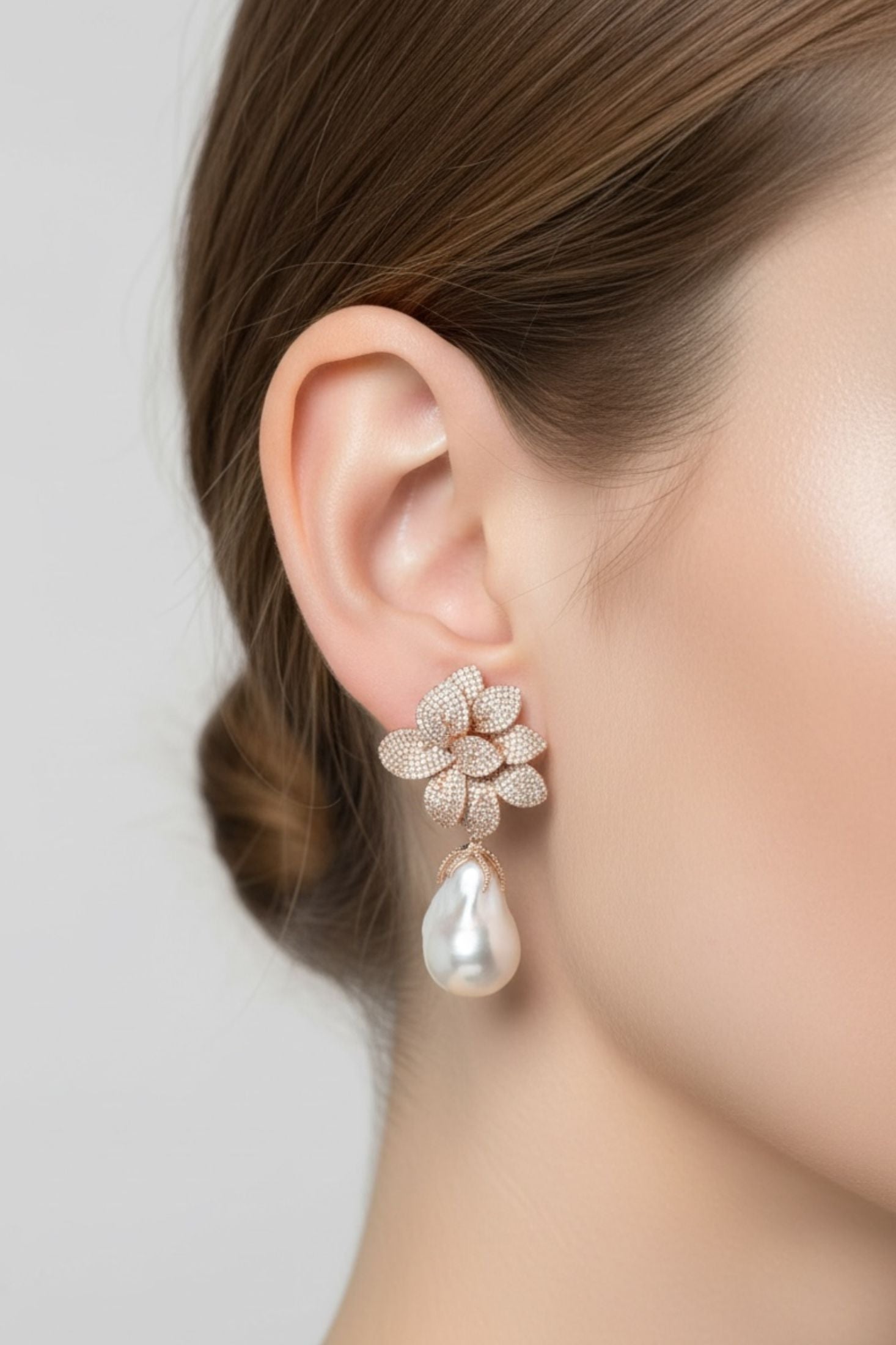 Close-up of a person wearing a floral earring with a pearl drop on a plain background