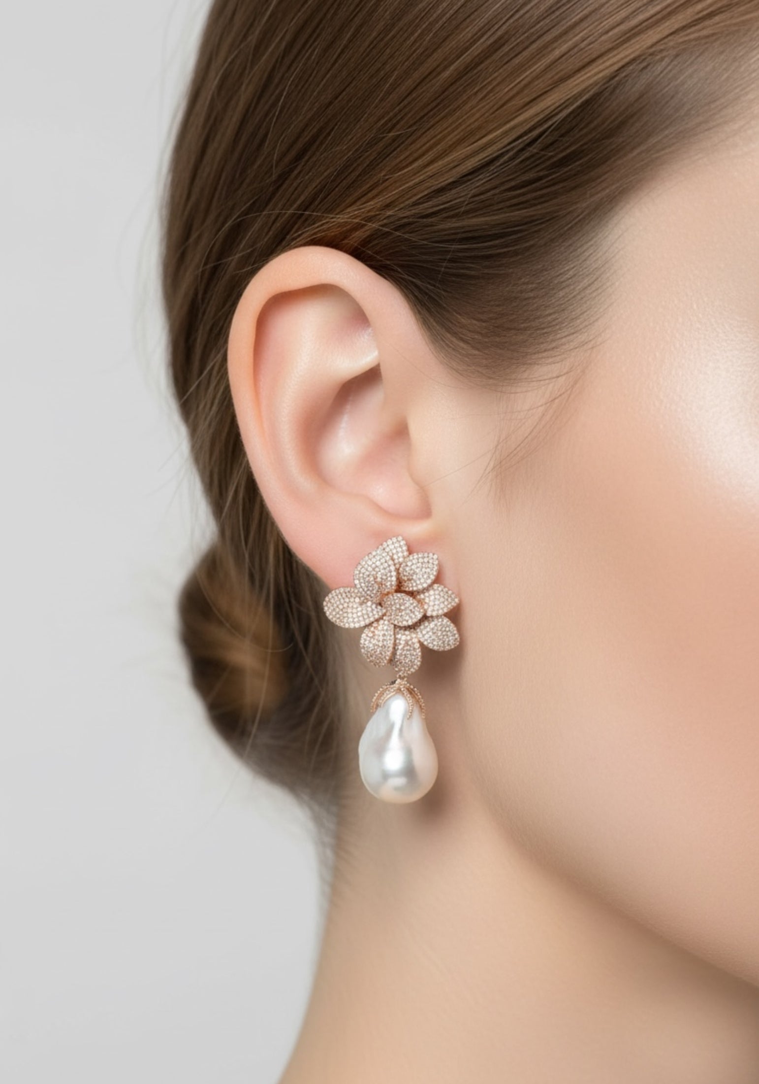 Close-up of a person wearing a floral earring with a pearl drop on a plain background