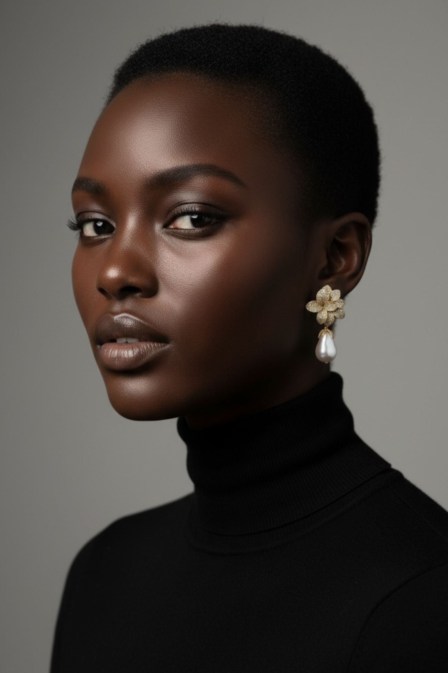 Woman wearing a black turtleneck and floral earrings against a gray background