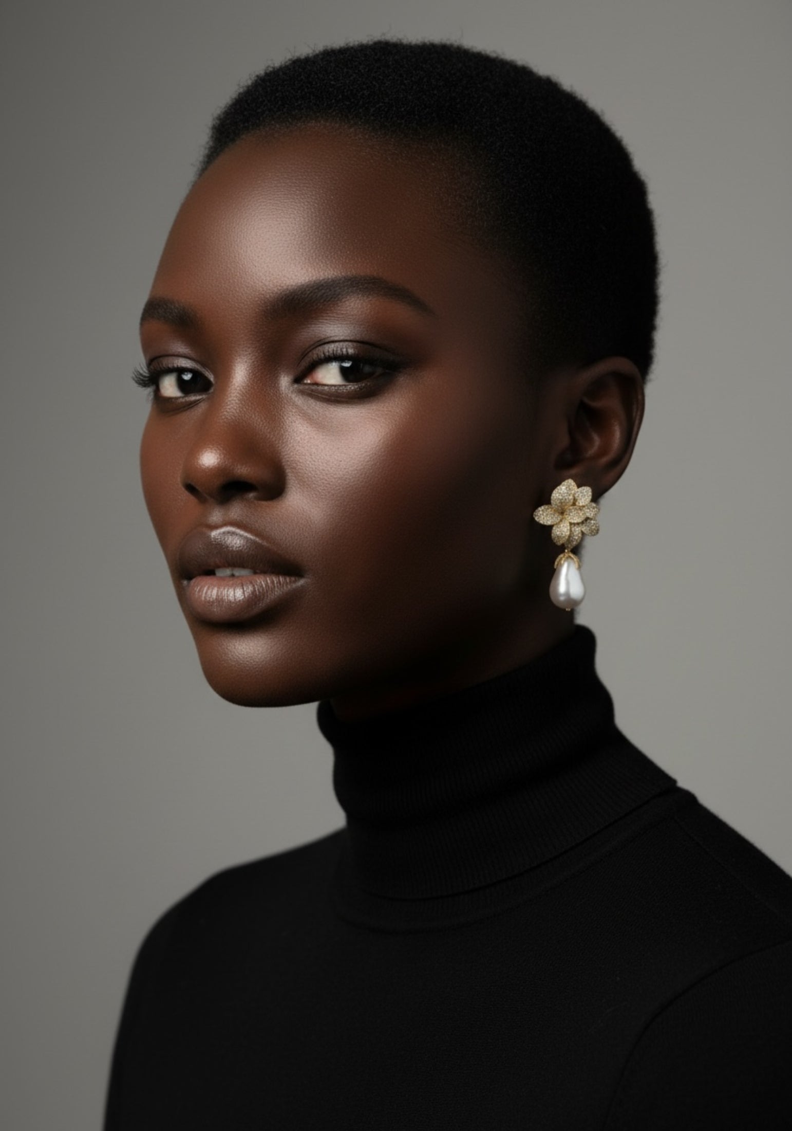 Woman wearing a black turtleneck and floral earrings against a gray background