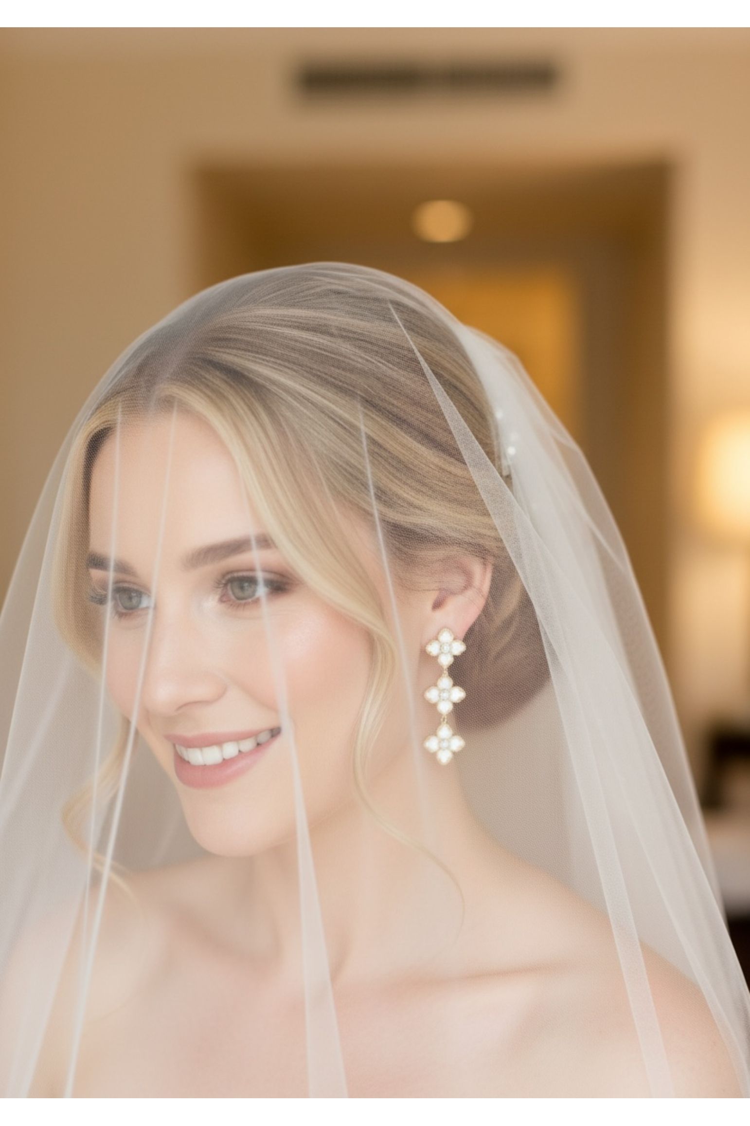 Bride wearing a veil and floral gold earrings with a blurred indoor background
