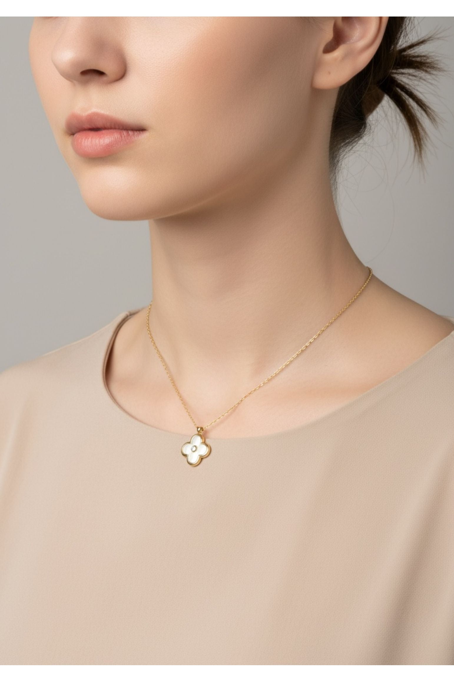 Woman wearing a gold necklace with a clover pendant against a neutral background