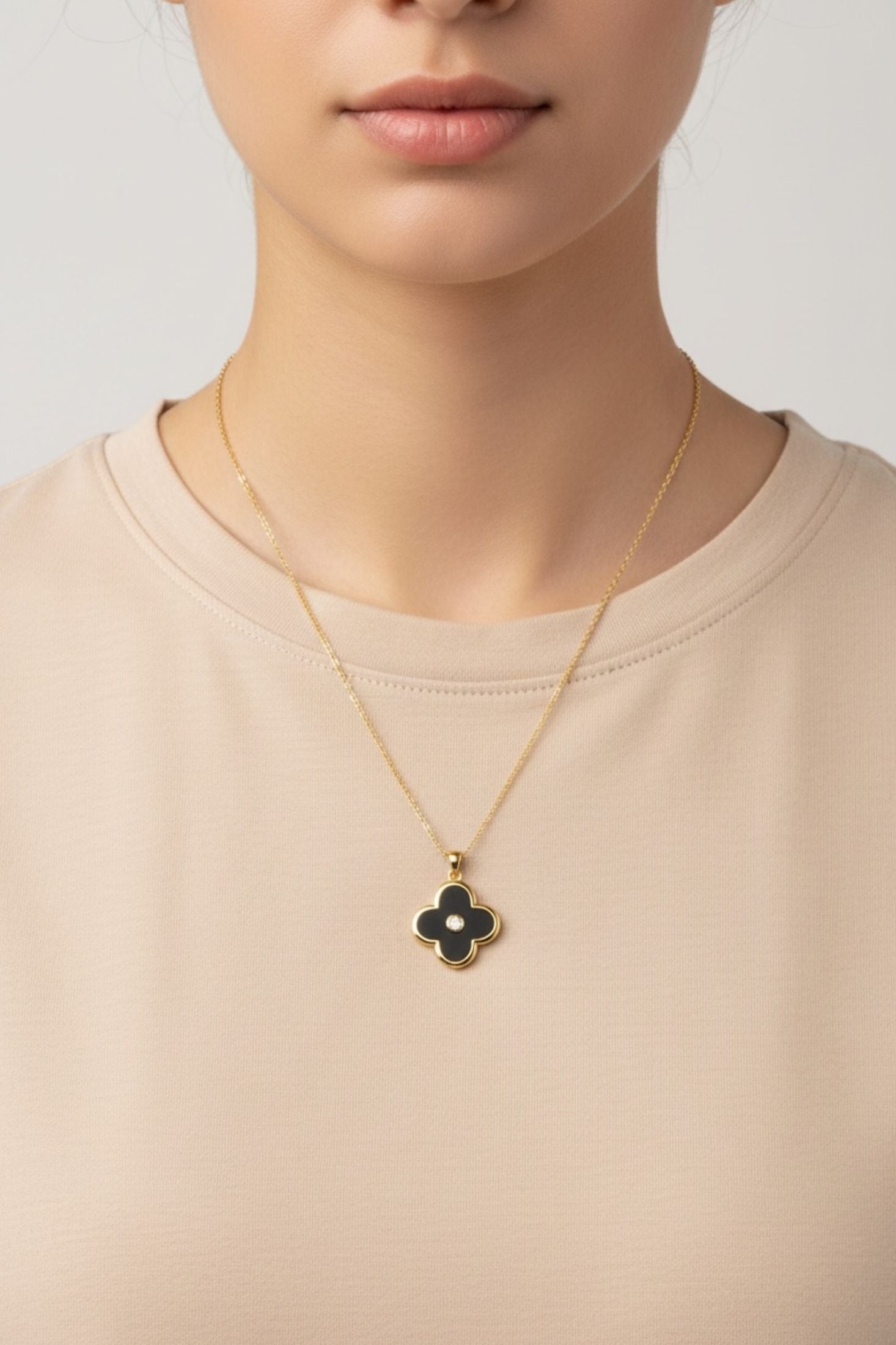 Gold necklace with a clover-shaped black pendant worn by a person in a beige shirt.