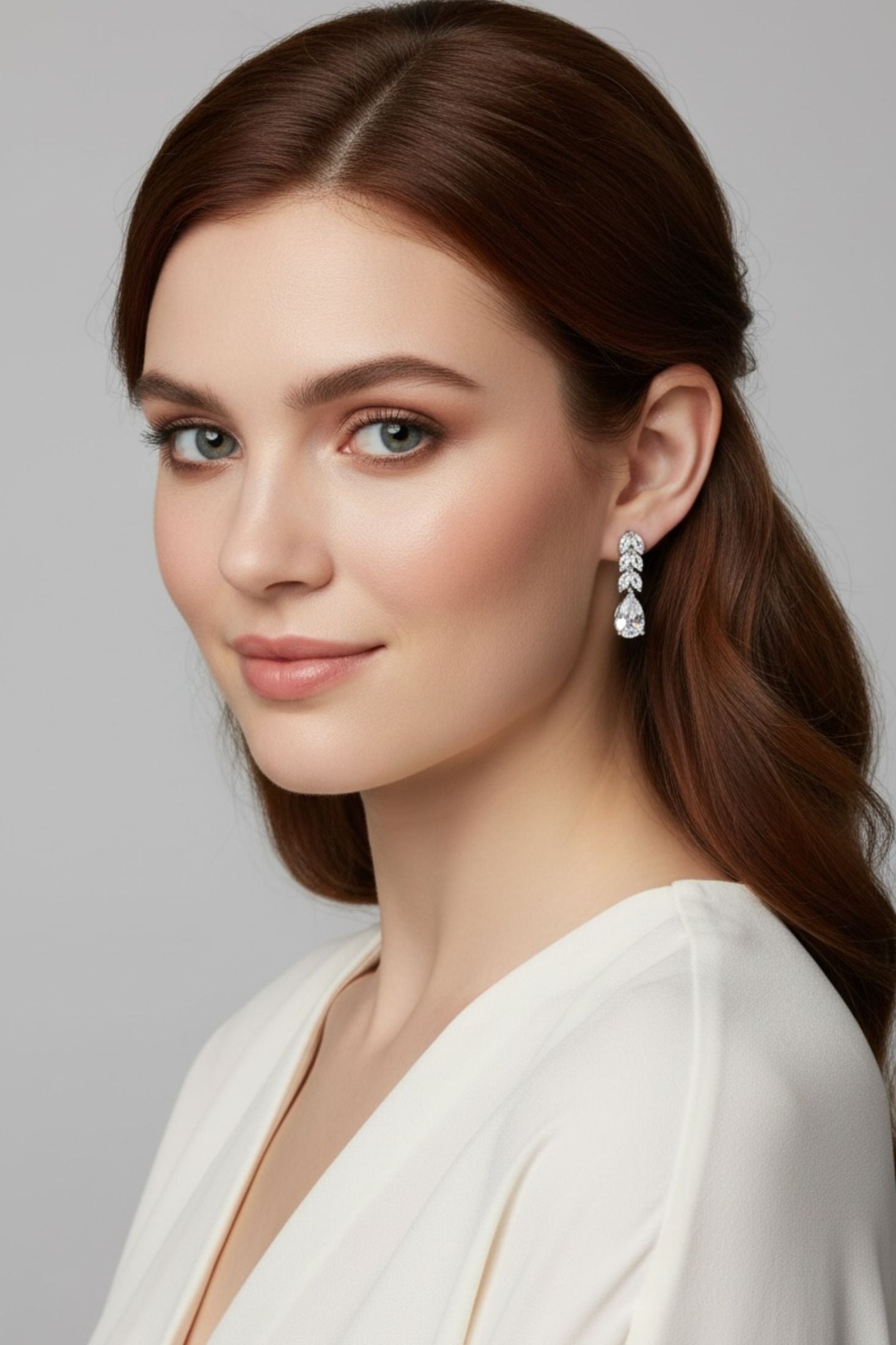 Woman in a white top wearing silver teardrop earrings with clear gemstones on a gray background