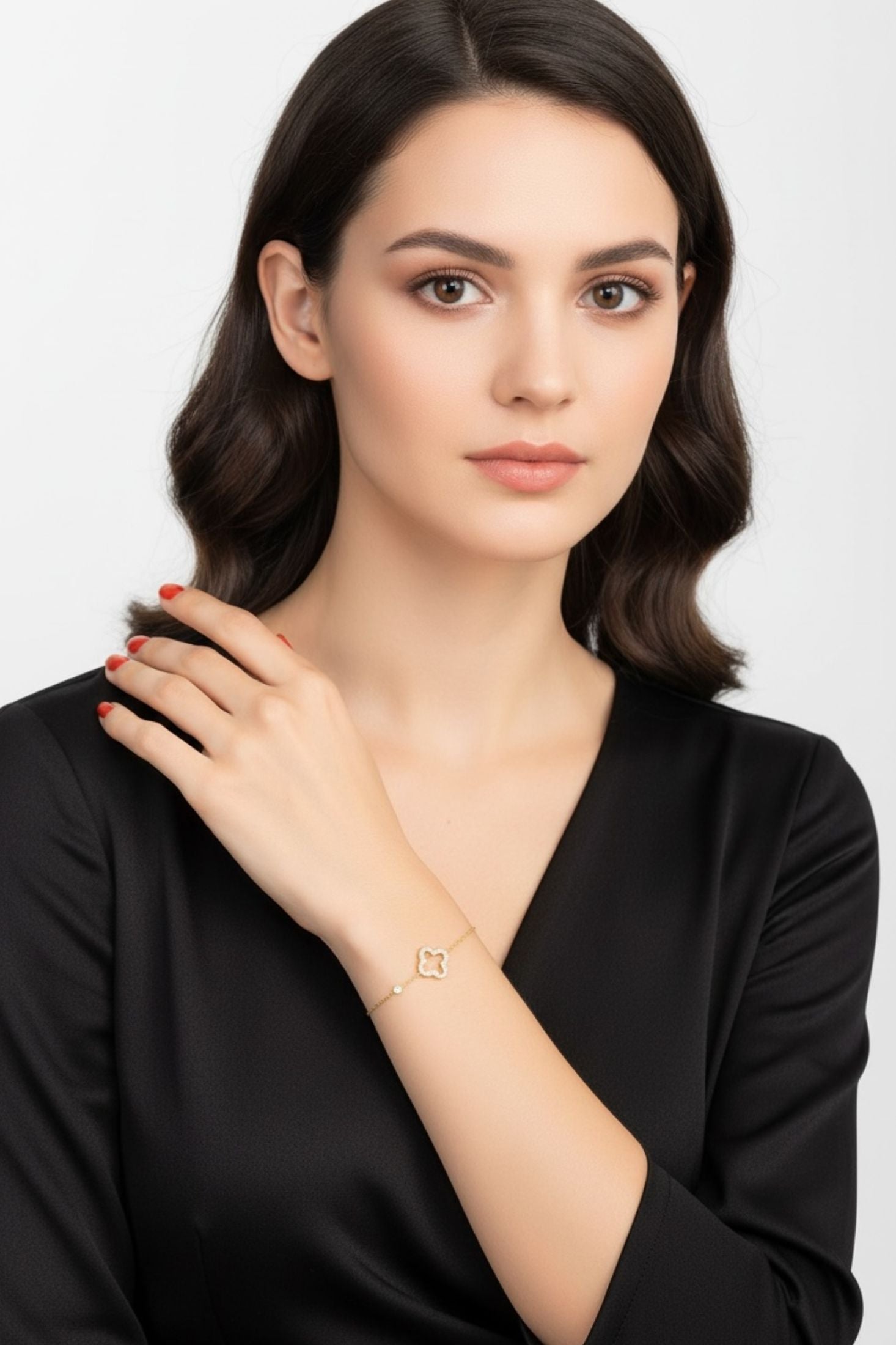 Woman wearing a gold clover bracelet on a plain background