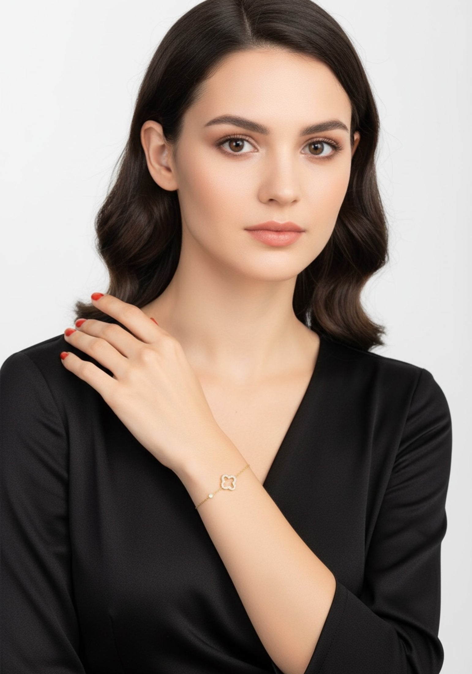 Woman wearing a gold clover bracelet on a plain background