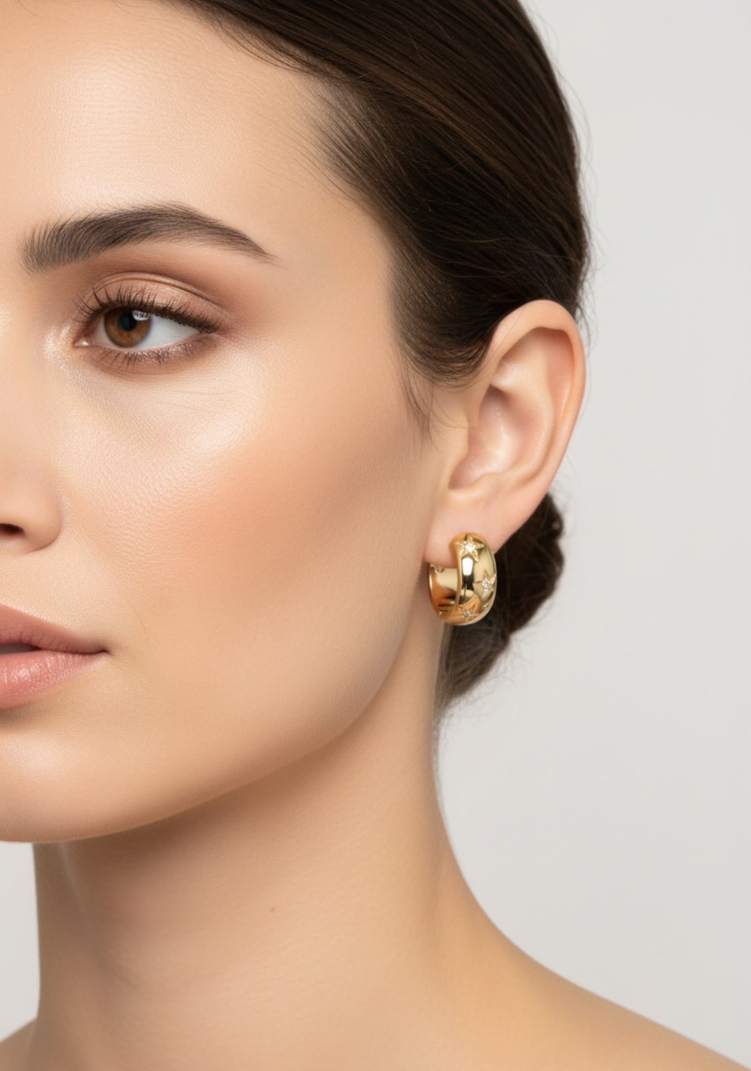 Close-up of a woman wearing gold hoop earrings against a neutral background