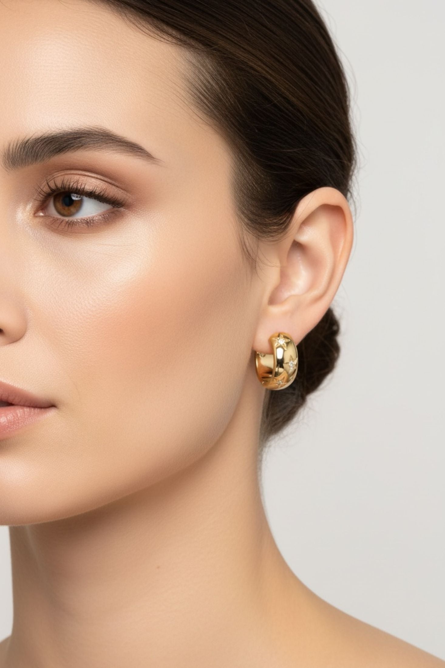 Close-up of a woman wearing gold hoop earrings against a neutral background