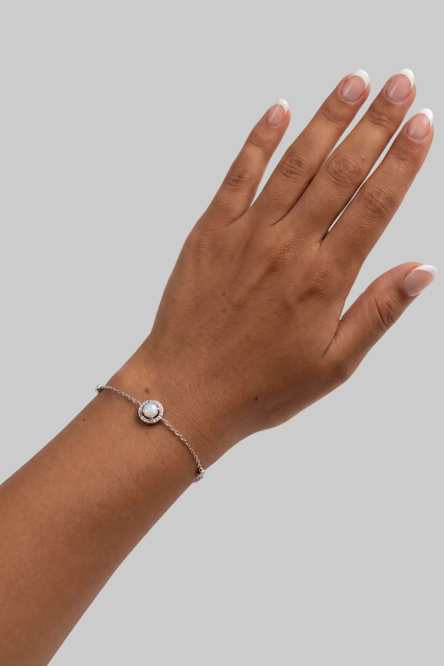 A delicate silver chain bracelet with a small oval bezel-set light blue stone, shown worn on a person's wrist against a clean white background.
