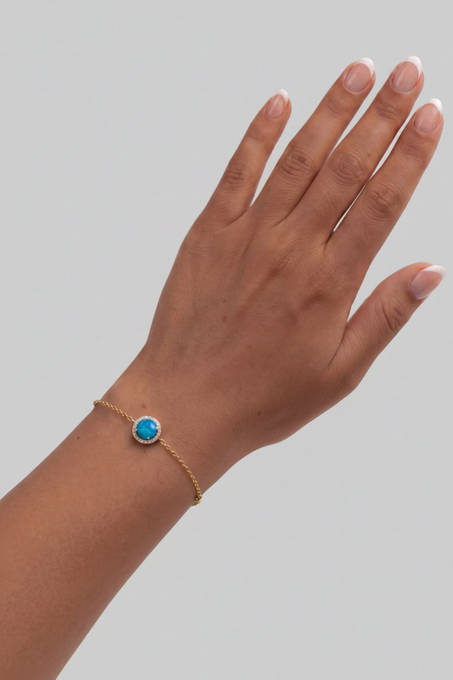 A gold chain bracelet with a round turquoise-blue stone bezel, shown worn on a person's wrist against a light off-white background.