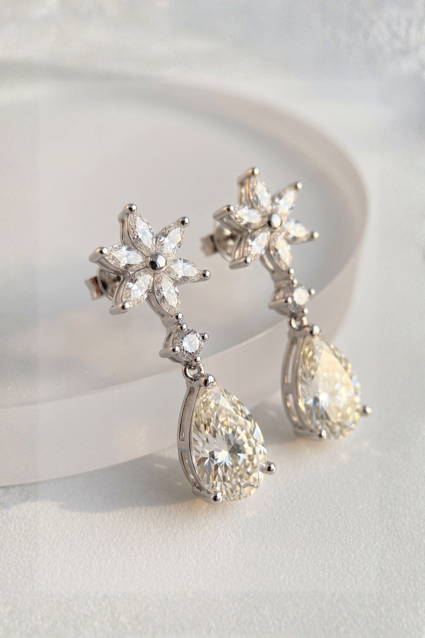 A pair of silver-toned dangle earrings with marquise-cut crystal flower motifs and teardrop-shaped clear crystals, displayed on a soft white surface.