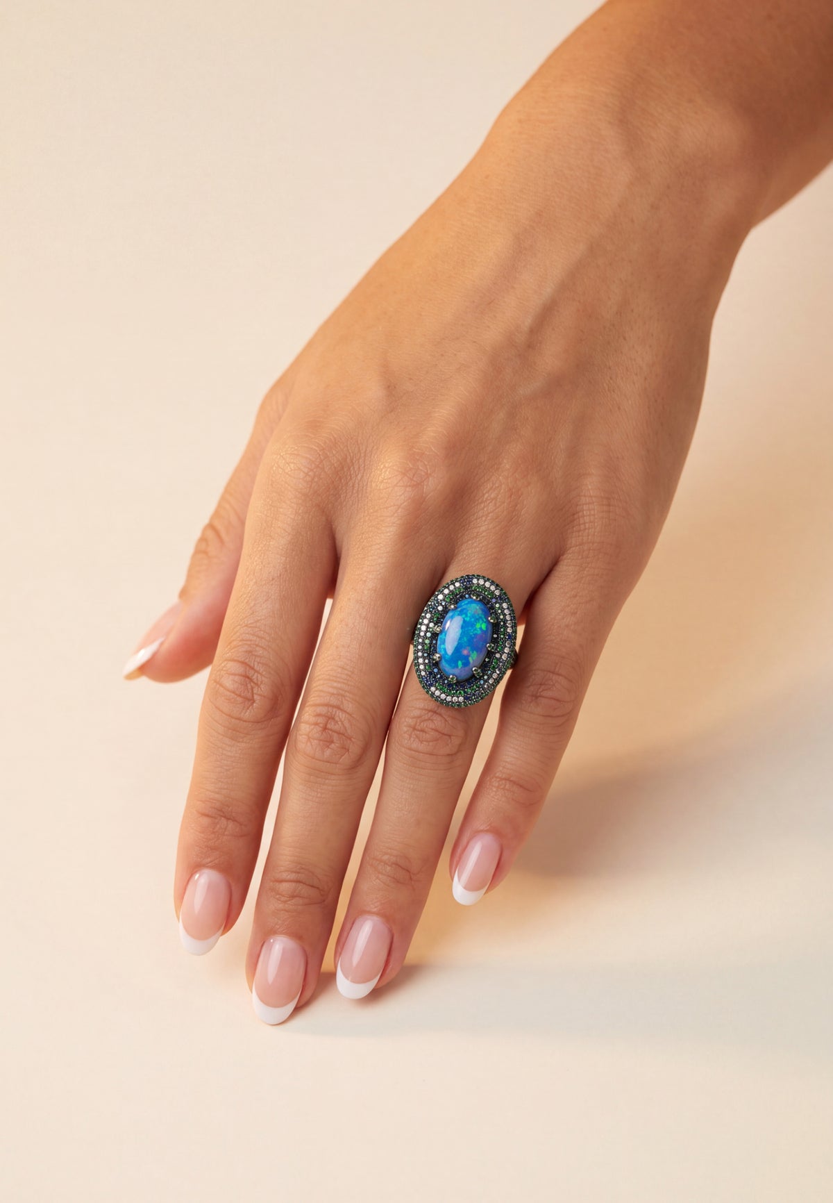 Hand wearing an oval blue opal ring with sparkling dark gemstone halo.