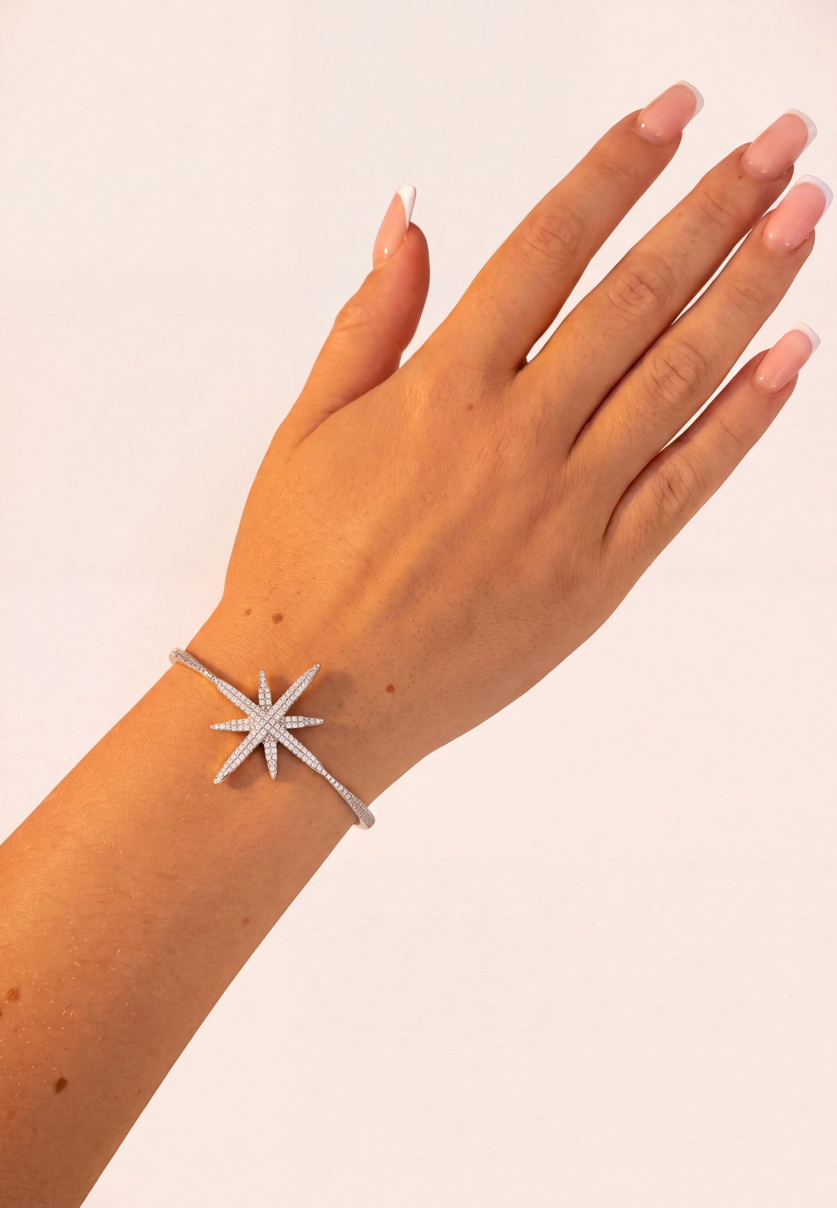 Hand wearing a silver star-shaped diamond tennis bracelet on a light background.