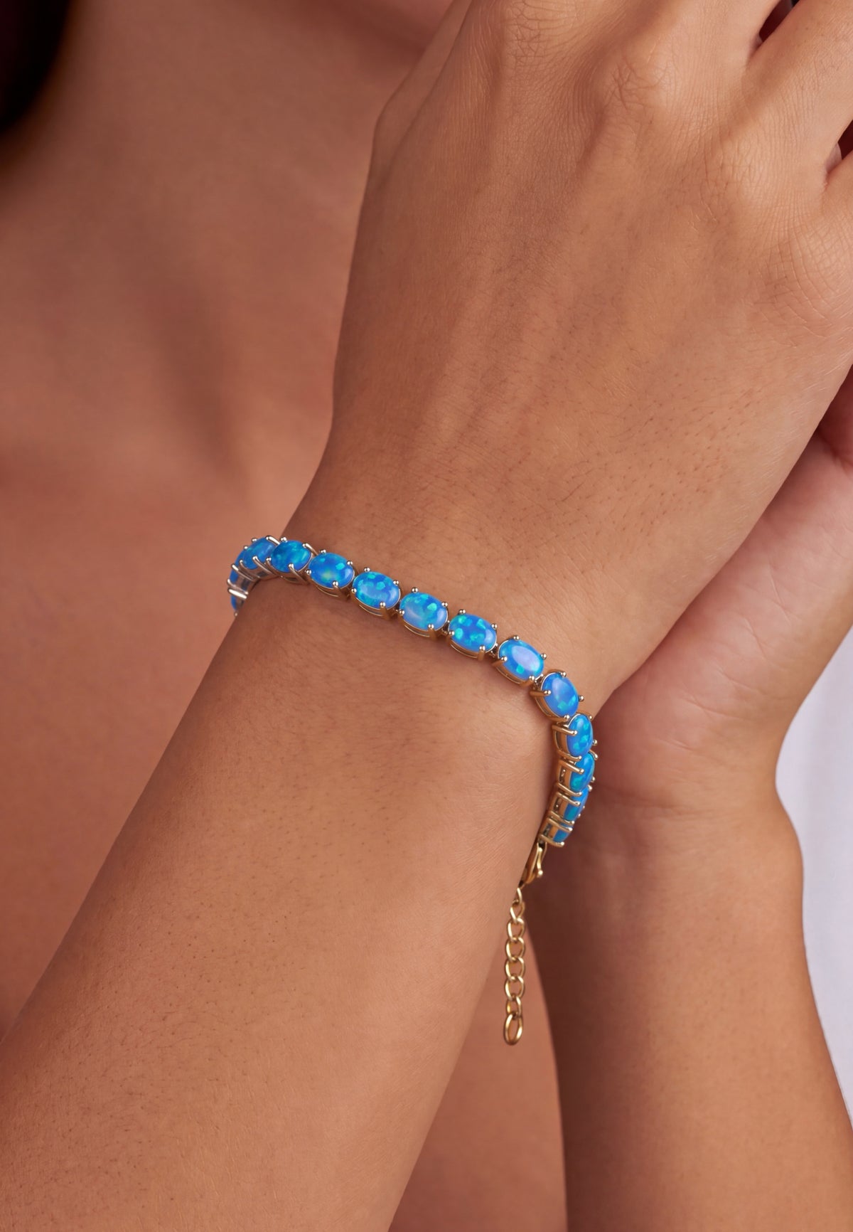 Close-up of a gold tennis bracelet with blue opal gemstones on a person's wrist.