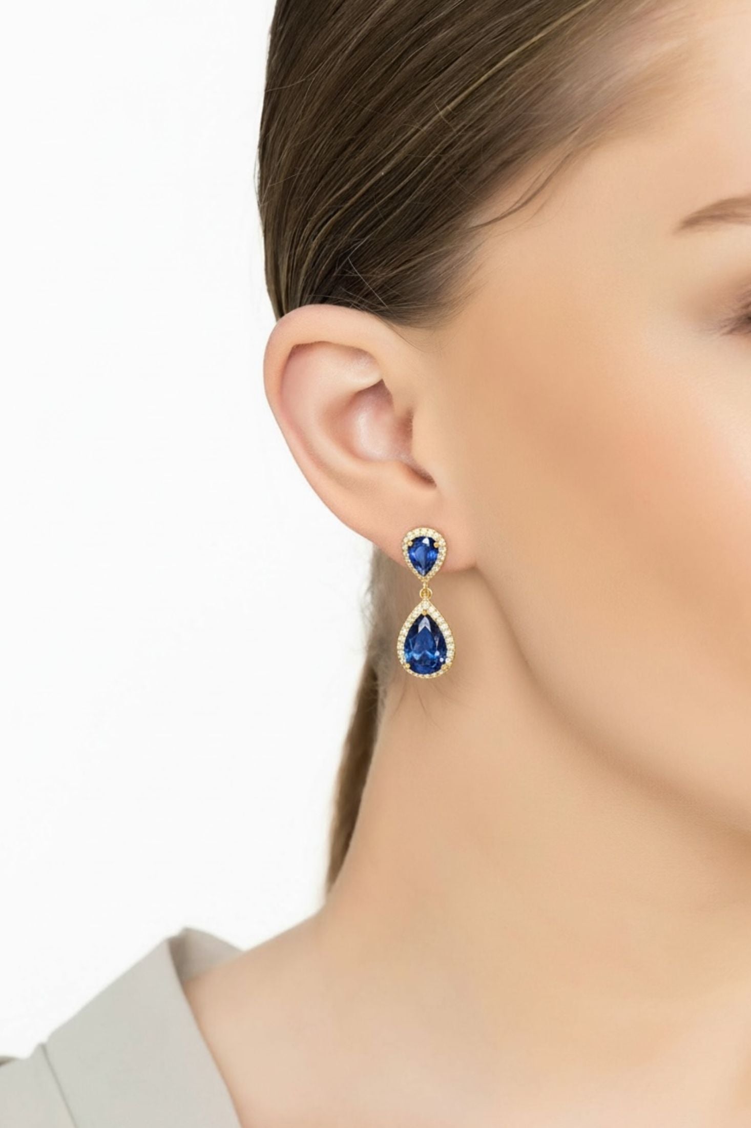 Close-up of a person wearing blue teardrop earrings with a neutral background