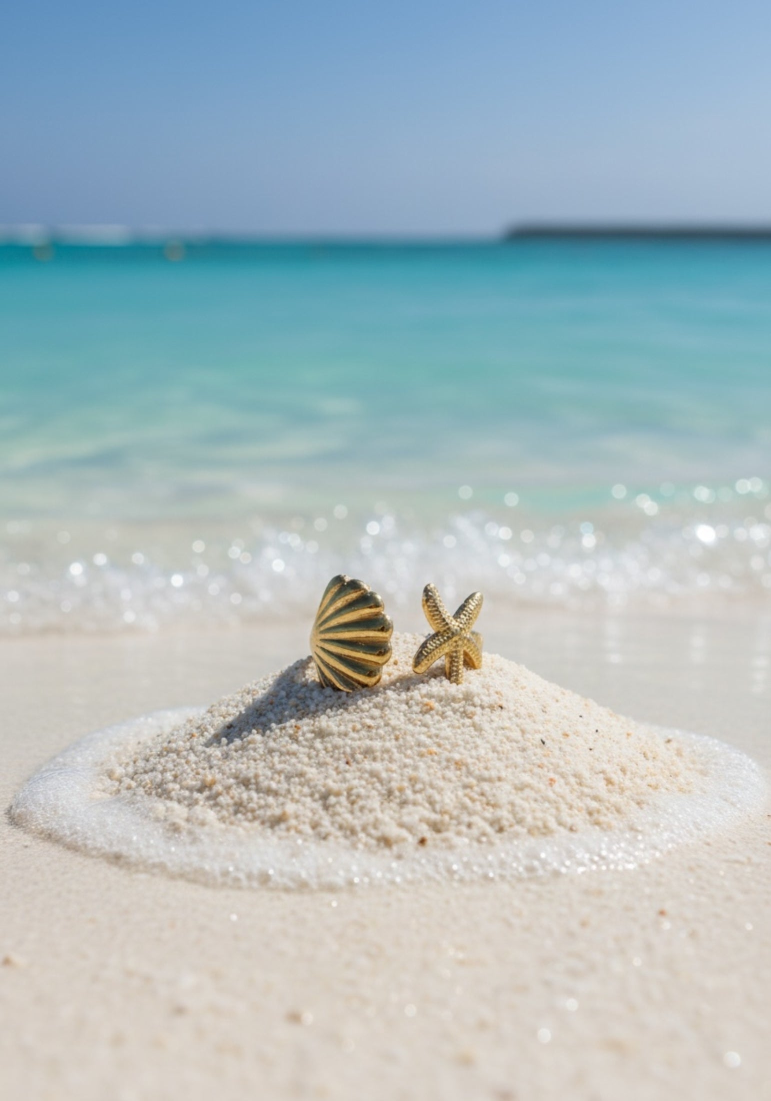 A gold ring with a starfish and shell on a clear blue water background