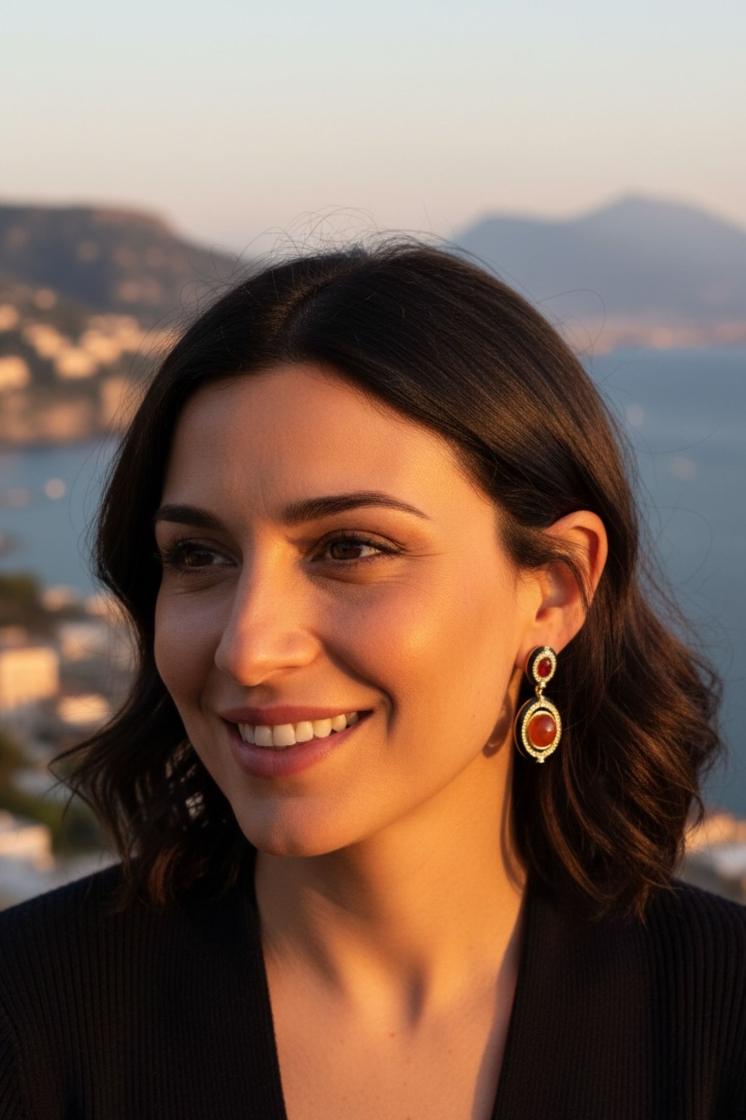 Woman with earrings against a scenic background of mountains and water.