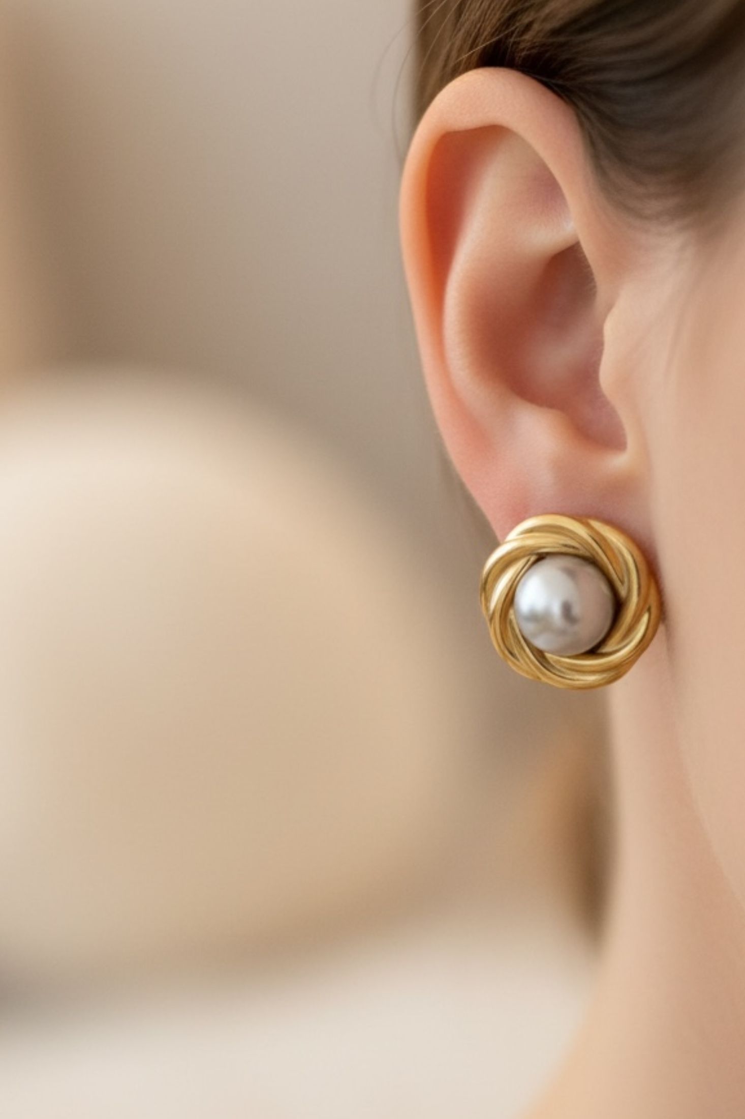 Gold earring with a pearl on an ear against a blurred background